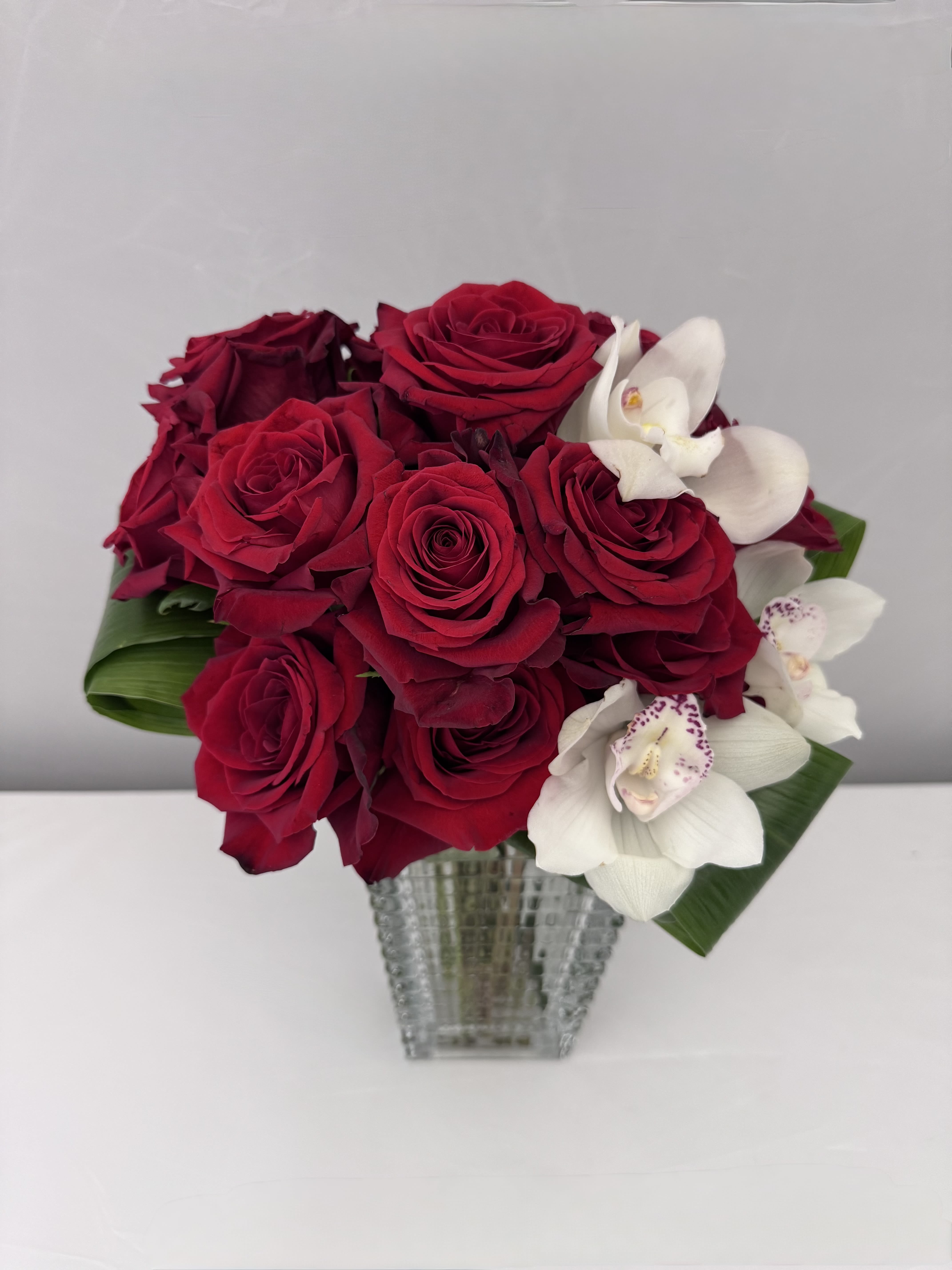 RED LUXE - RED LUXE IS AN ARRANGEMENT OF RED ROSES AND CYMBIDUM ORCHIDS DESIGNED IN A TAPERED, TEXTURED VASE THAT OFFERS A CAPTIVATING BLEND OF ELEGANCE &amp; CONTEMPORARY DESIGN. THE SERIFINA VASE IS MADE OF HIGH QUALITY GLASS &amp; IS A BEAUTIFUL ACCENT TO ANY HOME. (8.75HX4WX5.25L)  