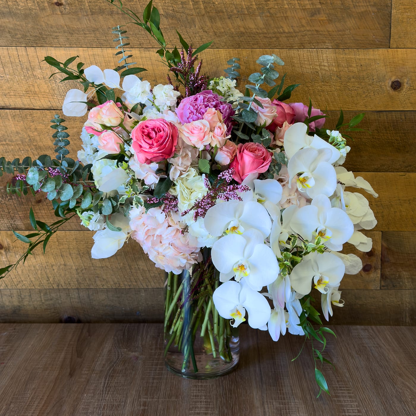 Rose Flow - Seasonal which contains Roses, Spray Roses, Eucalpytus, Italian Ruscus, Phalaenopsis Orchids, Hydrangeas, Peonie if in season, Dried Silver Dollar, Fillers, and Greenery