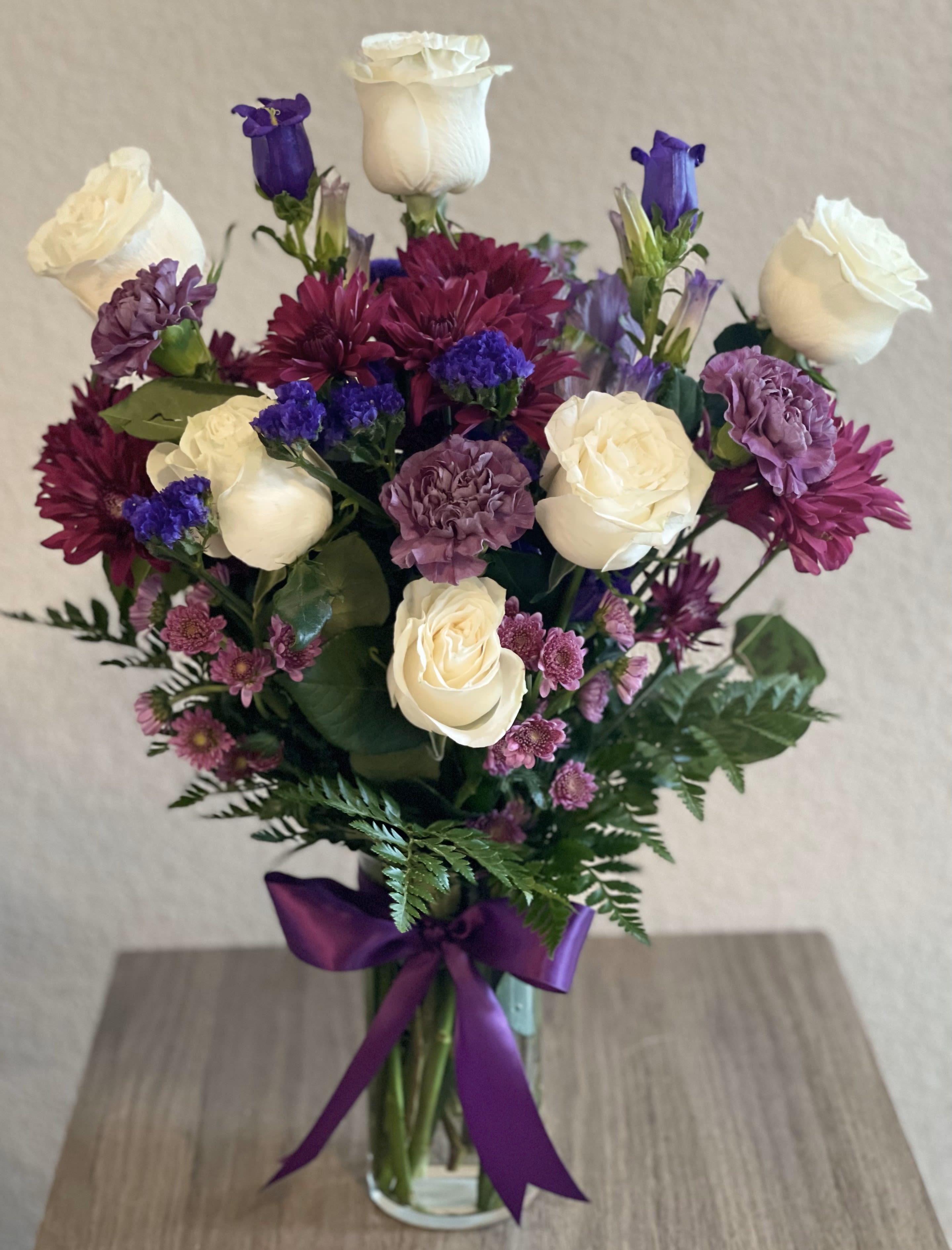 Mist of Memories Mist of Memories - Lovely flower arrangement of white roses, purple carnations, mix color of mums, purple campanula bellflowers and leather leaves on a clear vase with an elegant bow.