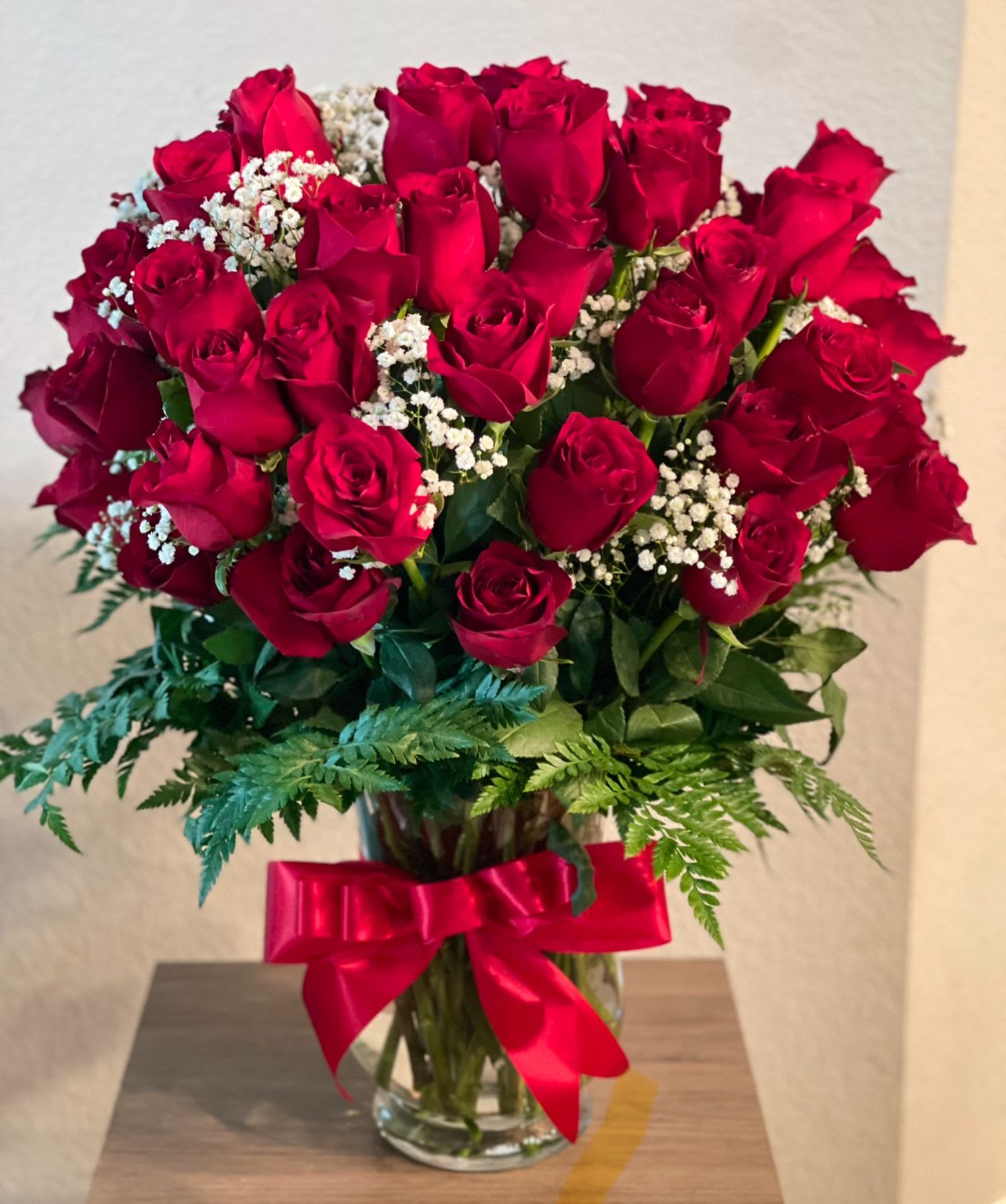 Glamorous Red  - Marvelous arrangement of 60 long stem red roses with baby’s breath and assorted greenery all around on a tall clear glass vase with an elegant bow.