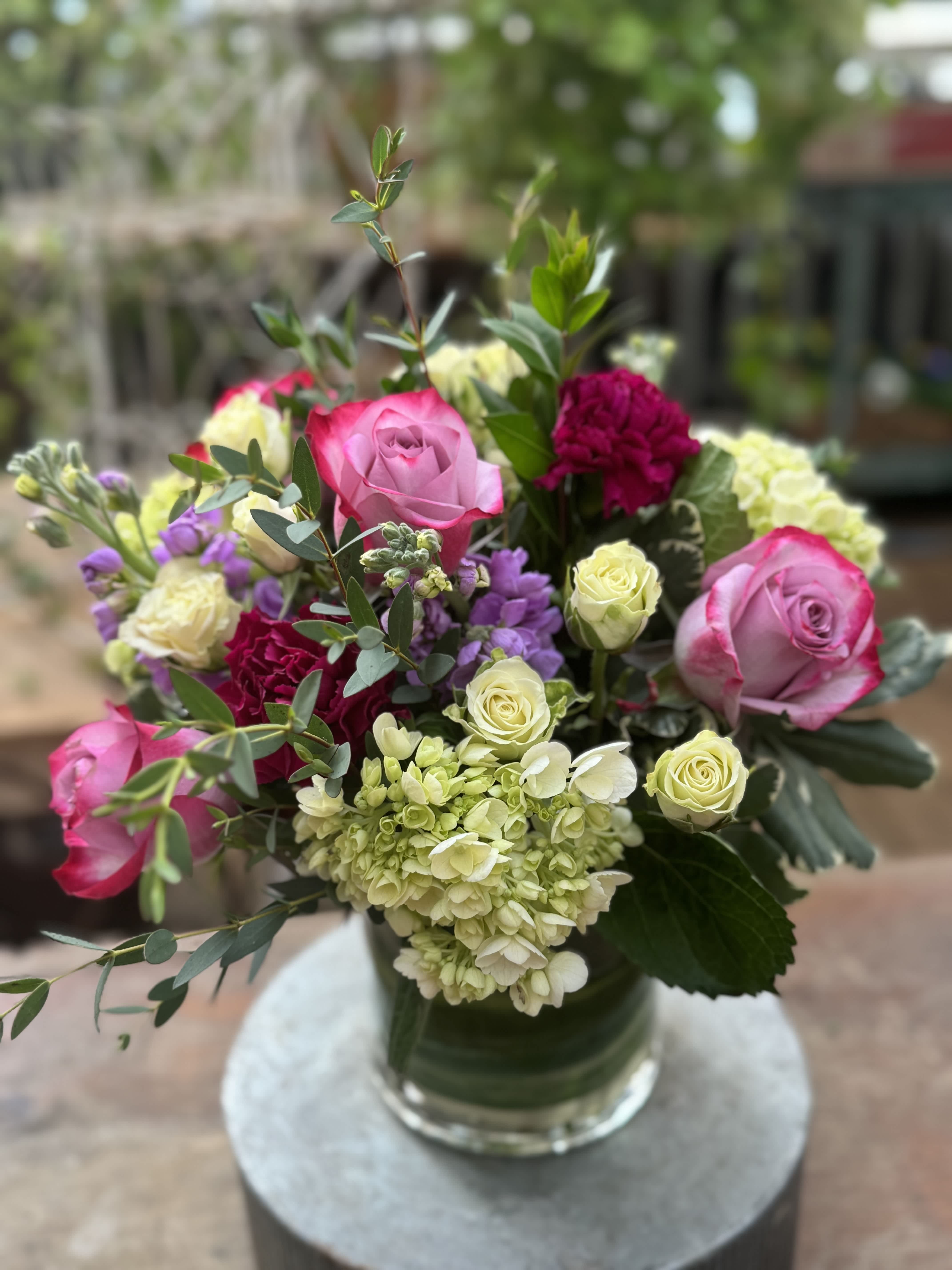 Purple and Green Designers Choice  - A beautiful and delicate display of in season purple and green blooms arranged low and lush with premium greens. Design is subject to change based on seasonal availability but will include flowers such as roses, stock, hydrangea, carnations, spray roses and soft greens. Express your occasion with a heartfelt bouquet of purple and green.