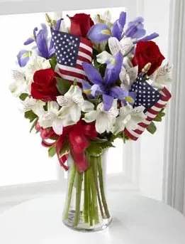 Unity Bouquet - Celebrate the day with a fresh and beautiful flower bouquet. This dazzling arrangement of patriotic red, white and blue flowers sends a statement of hope and strength to your recipient.  The Unity Bouquet is a noble bouquet, brimming with red roses, blue iris, white Peruvian lilies and fresh greens. Overflowing with love for our country, this beautiful mix of patriotic colors is topped off with 2 small American Flags, a perfect touch when expressing your feelings of pride and joy. Your local florist uses only the freshest flowers available and will carefully place them into a gathering vase, wrapped in a bright red ribbon.  