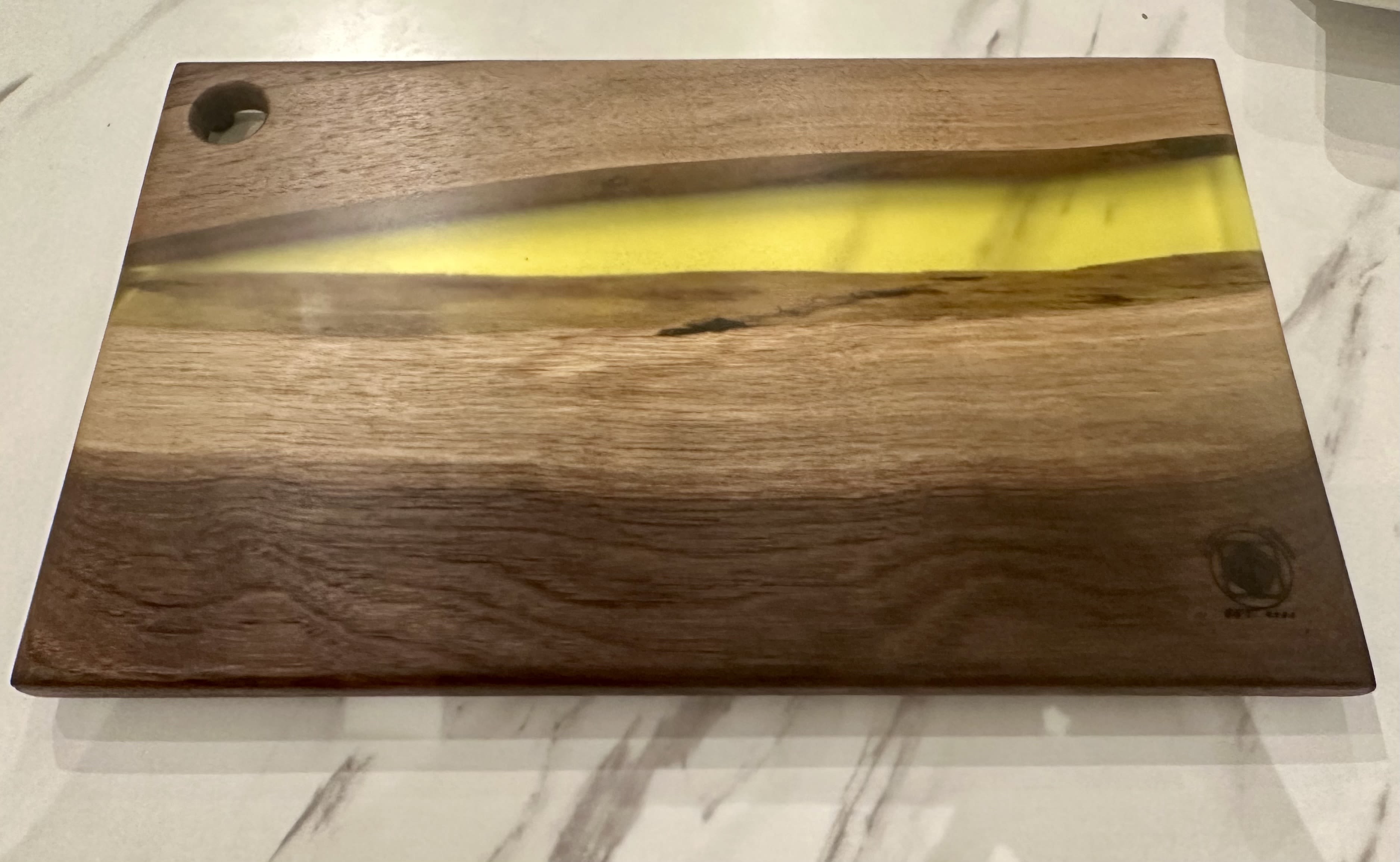 Medium Wood &amp; Epoxy Resin Cheeseboard - Add a touch of artistry to your entertaining with this elegant handcrafted wood and resin cheese board. Measuring 15.5&quot; x 9&quot;, this medium-sized board is perfect for serving an array of cheeses, charcuterie, fruits, and more. The board is made from premium walnut wood, showcasing its rich, natural grain, and is accented with a striking resin inlay available in four vibrant colors: blue, green, brown, and pink+blue. The resin inlay creates a beautiful contrast against the warm wood tones, giving the board a modern yet earthy aesthetic. Each piece is handmade with care, ensuring that no two boards are exactly alike. The artisan's mark is subtly engraved on the corner, adding a personal touch to this functional work of art.  Exclusively made for Chartruese by Roje by Dapperwood Atelier.