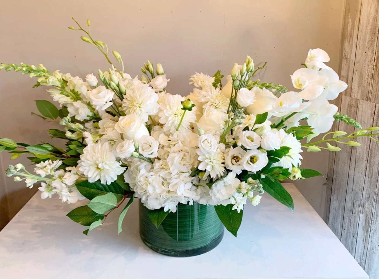 Monet - Monet is a lush gathering of all white premium blooms, featuring lisianthus, hydrangeas, roses, dahlias (if in season), and Phalaenopsis orchids accented greenery. 