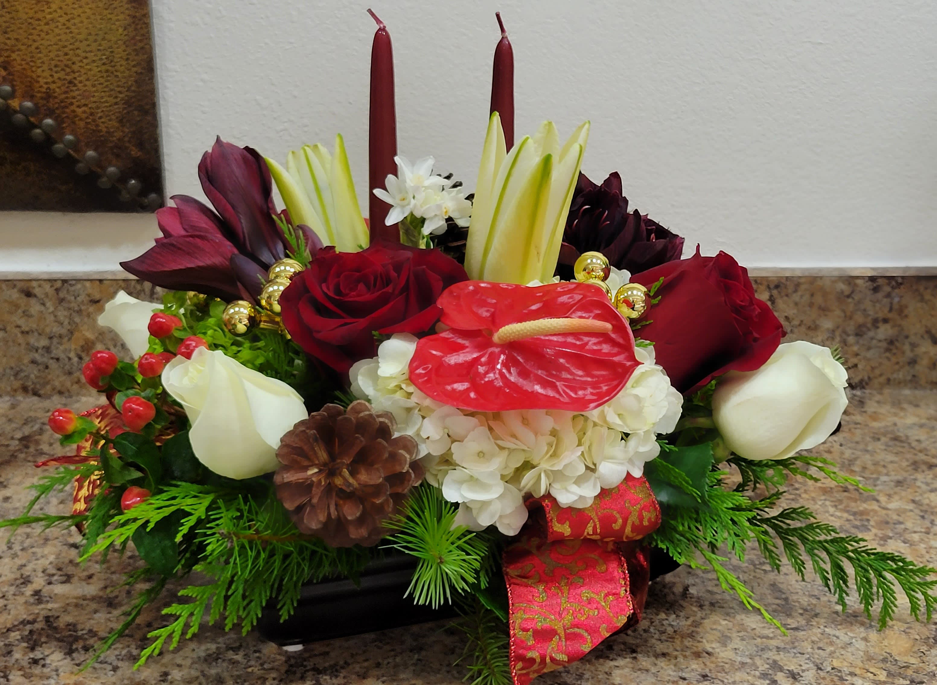 Holiday Glow Centerpiece - Christmas centerpiece long and low suitable for you and your Christmas celebration. this beautiful centerpiece made with fragrant burgundy &amp; white roses and spray rose, beautiful burgundy and green cymbidiums orchids green, red anthurium, white hydrangea, and Christmas greens decorated with 2 red candles, bulbs and red velvet ribbon  Flowers &amp; Elements Included:      Deep Red Roses     White Roses     Burgundy Amaryllis     Red Anthurium     White Hydrangeas     Elegant White Lilies     Festive Red Candles     Pinecones and Seasonal Greenery     Decorative Gold Ornaments and Red Ribbon  Illuminate your holiday celebrations with the &quot;Holiday Glow Centerpiece,&quot; an elegant arrangement that embodies the warmth and beauty of the season. Featuring rich red roses, burgundy amaryllis, and delicate white lilies, this stunning floral piece is accented with festive touches like pinecones, golden ornaments, and seasonal greenery. Two glowing red candles add a cozy and magical ambiance, making it the perfect centerpiece for Christmas gatherings, winter celebrations, and holiday feasts.  Spread the joy of the season with this luxurious floral masterpiece!
