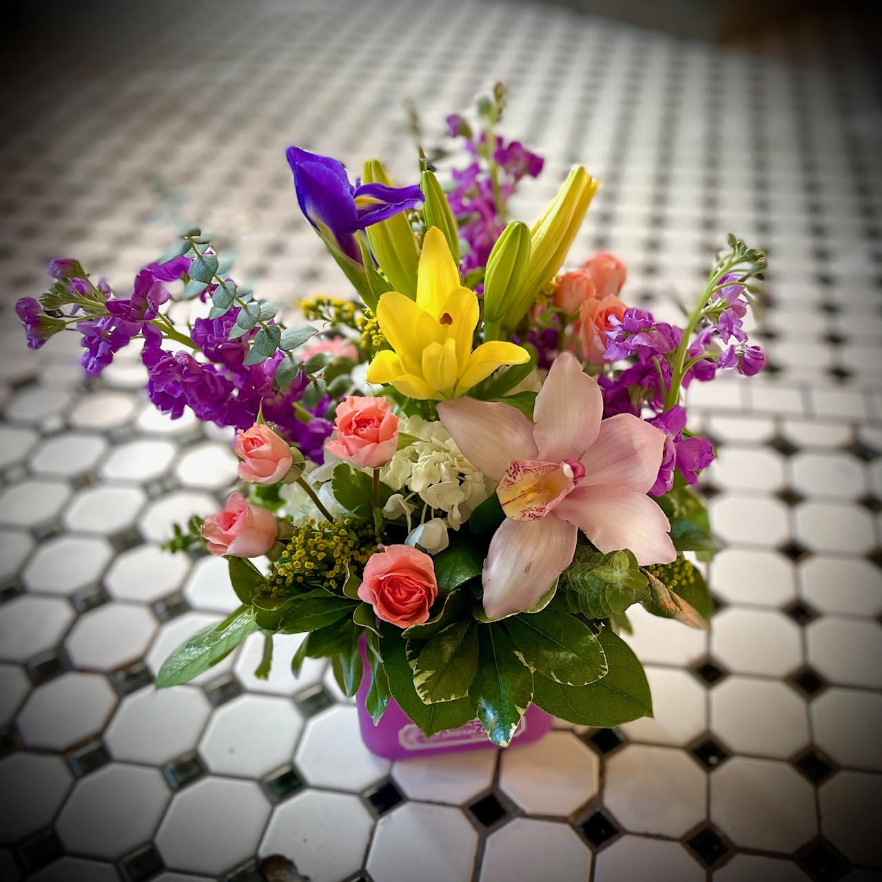 Soft Serenity - The Soft Serenity design is perfect to design to bring Zen with it's display of yellow lilies, a pink cymbidium orchid, purple stock, iris, soft pink spray roses, and a touch of eucalyptus. This arrangement is perfect to bring peace to any home or office space