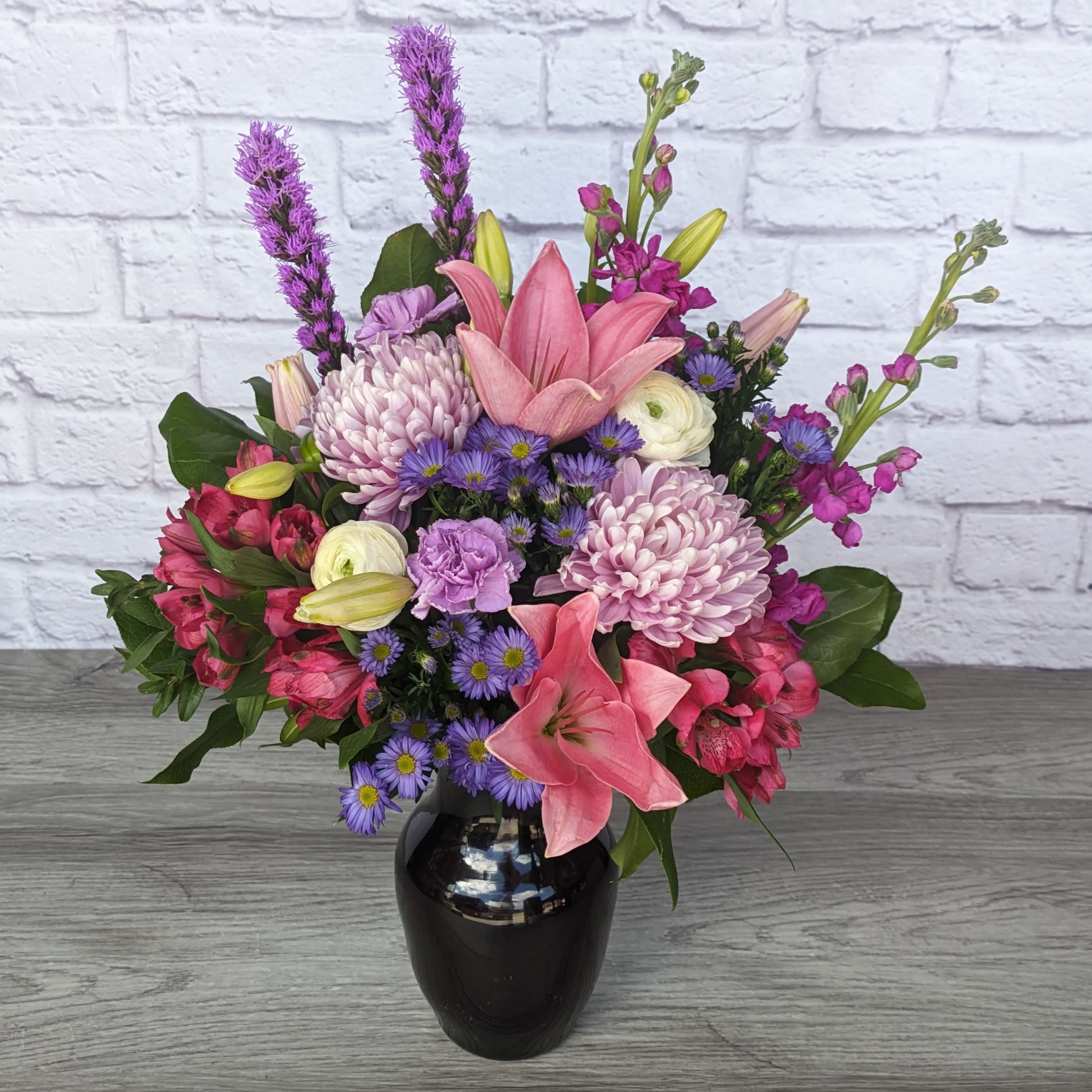 Tutti Frutti - Tutti Frutti is A Ladybug Floral exclusive bouquet. Once only offered for a month but by popular demand is a permanent year long bouquet. This bouquet includes lilies, stock, liatris, football mums, ranunculus, alstroemeria, carnations and monte casino aster, all within an 8” plum rose vase. Shout out to Brandie for naming this month's bouquet. If you would like the chance to name next month's special, follow us on Facebook or Instagram and earn your chance to get a free bouquet!  One Sided Orientation 21&quot;H X 16&quot;W 