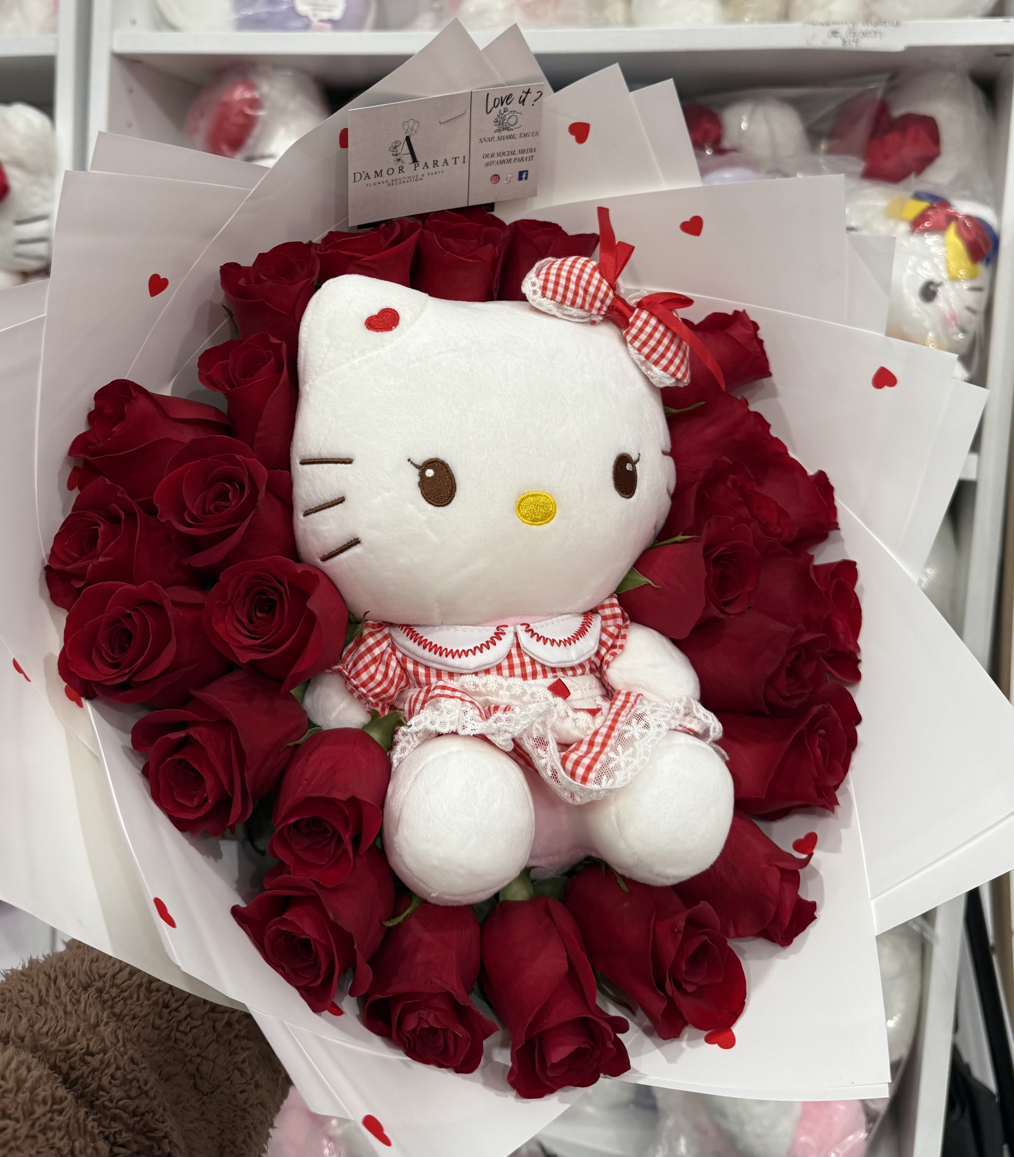 Red lover Hello Kitty Red lover Hello Kitty - A bouquet of red roses surrounds a Hello Kitty plush toy, creating a lovely gift arrangement. The bouquet is composed of many deep red roses, tightly packed together, filling most of the image. The roses are arranged artfully, suggesting a well-crafted floral design. A white wrapping paper with small red hearts dotted on it is visible beneath and around the roses. The Hello Kitty plush toy is positioned centrally within the bouquet. It's a light white, sitting amongst the roses and wearing a red and white checkered dress. The Hello Kitty plush toy is the central subject, featuring its recognizable cartoonish design and charming expression. The plush toy is a common, popular collectible, and its recognizable design adds to the image's overall theme. The roses are the primary visual element surrounding the Hello Kitty plush, creating a pleasing contrast of textures and colors. The roses are deep red in color, with vibrant tones that complement the white of the Hello Kitty plush.