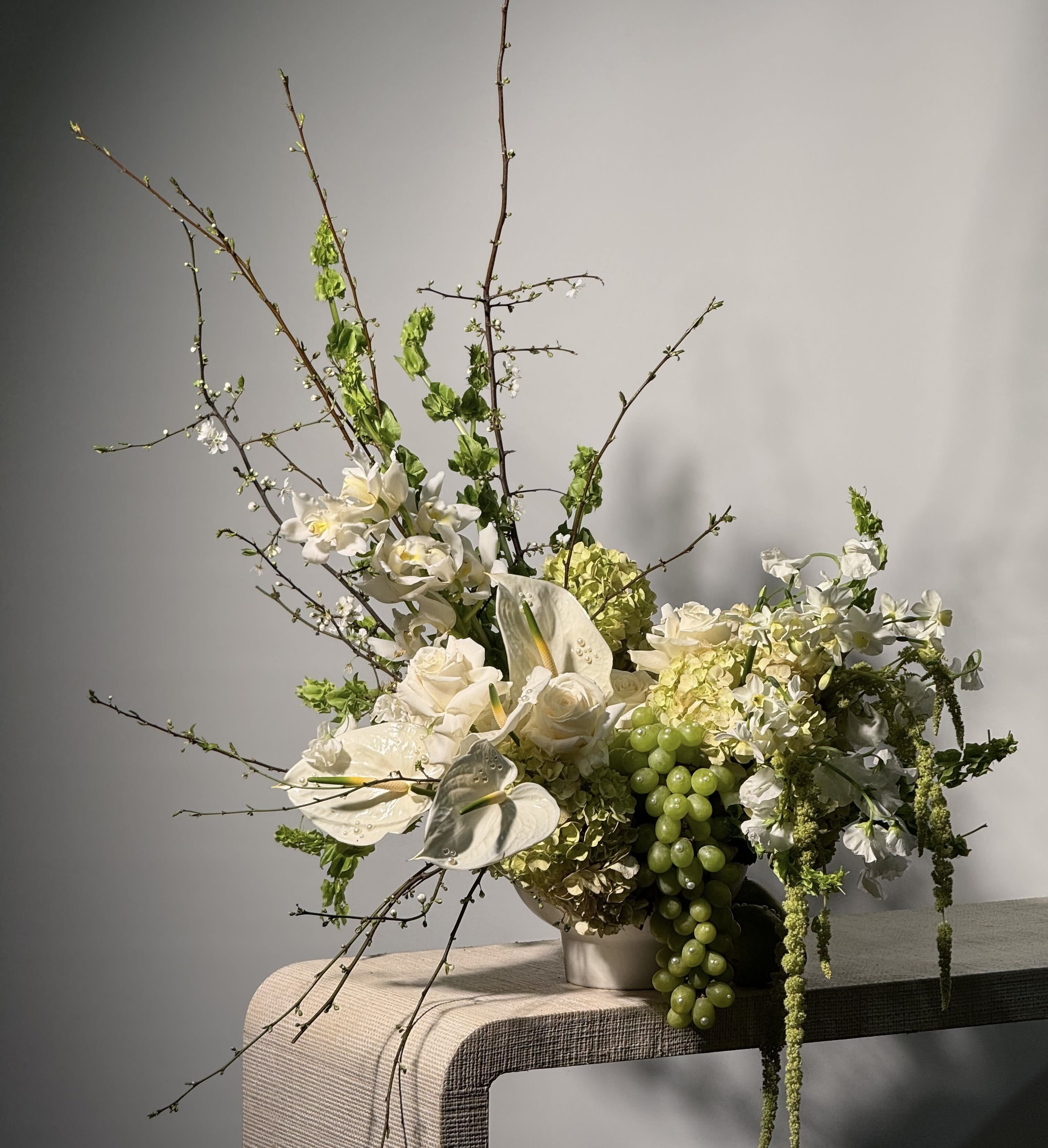 THROUGH THE GRAPEVINE - - A calming mix of crisp white and lush green tones for a modern, timeless look. -  Earthy brown branches create contrast and a touch of organic texture. - An arrangement that brings nature’s beauty indoors with understated sophistication.  