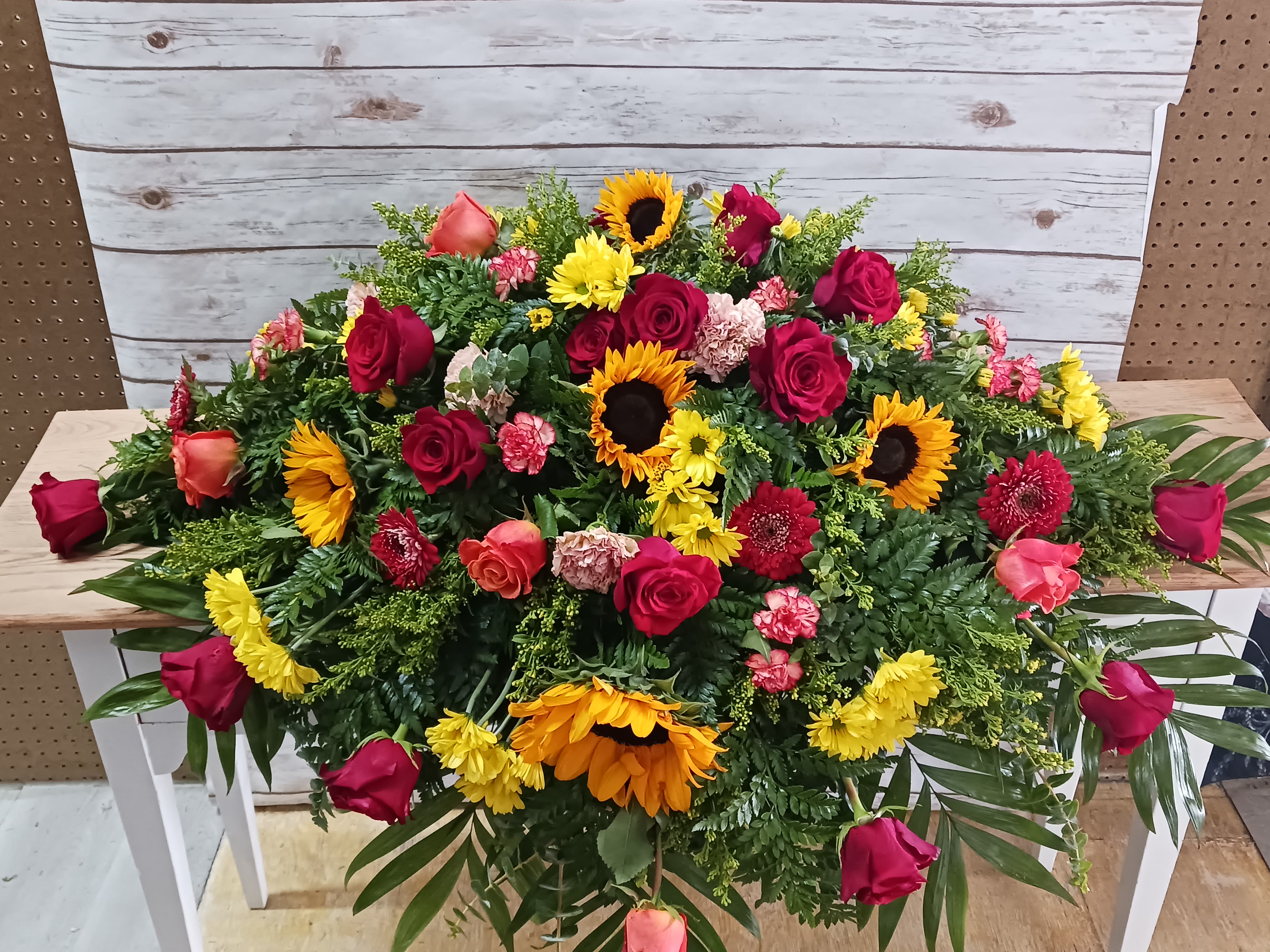 Garden at Sunset Garden at Sunset - Lovely casket spray to honor your loved one. Includes a variety of flowers to include sunflowers, roses, daisies and carnations.