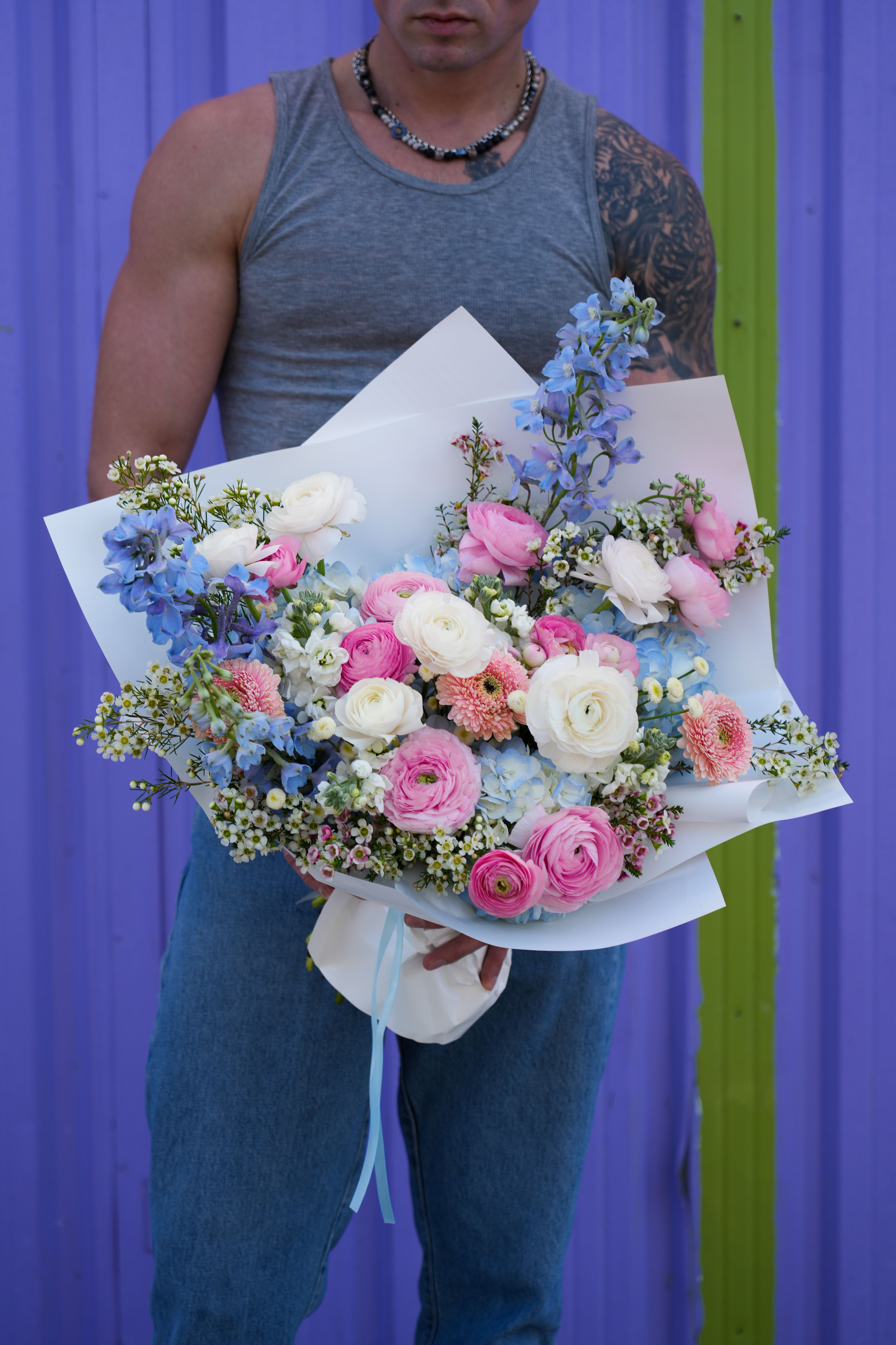 Serene Pastels Bouquet - A delicate and dreamy bouquet that captures the essence of elegance and romance. Featuring lush white ranunculus, soft pink ranunculus, pastel blue hydrangeas, vibrant blue delphiniums, and charming pink chrysanthemums, this arrangement is a perfect harmony of colors and textures. Accented with wax flowers and other seasonal blooms, it’s beautifully wrapped in crisp white paper and finished with a flowing blue ribbon. Ideal for birthdays, anniversaries, baby showers, or any occasion that calls for a touch of grace and beauty.