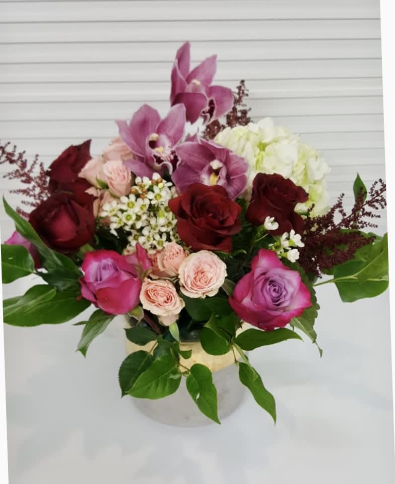 Joyful - A contemporary collection of Cymbidium Orchids, Hydrangea, Roses, surrounded by variety of lush fillers and greenery, in a concrete vase with gold embelishment.