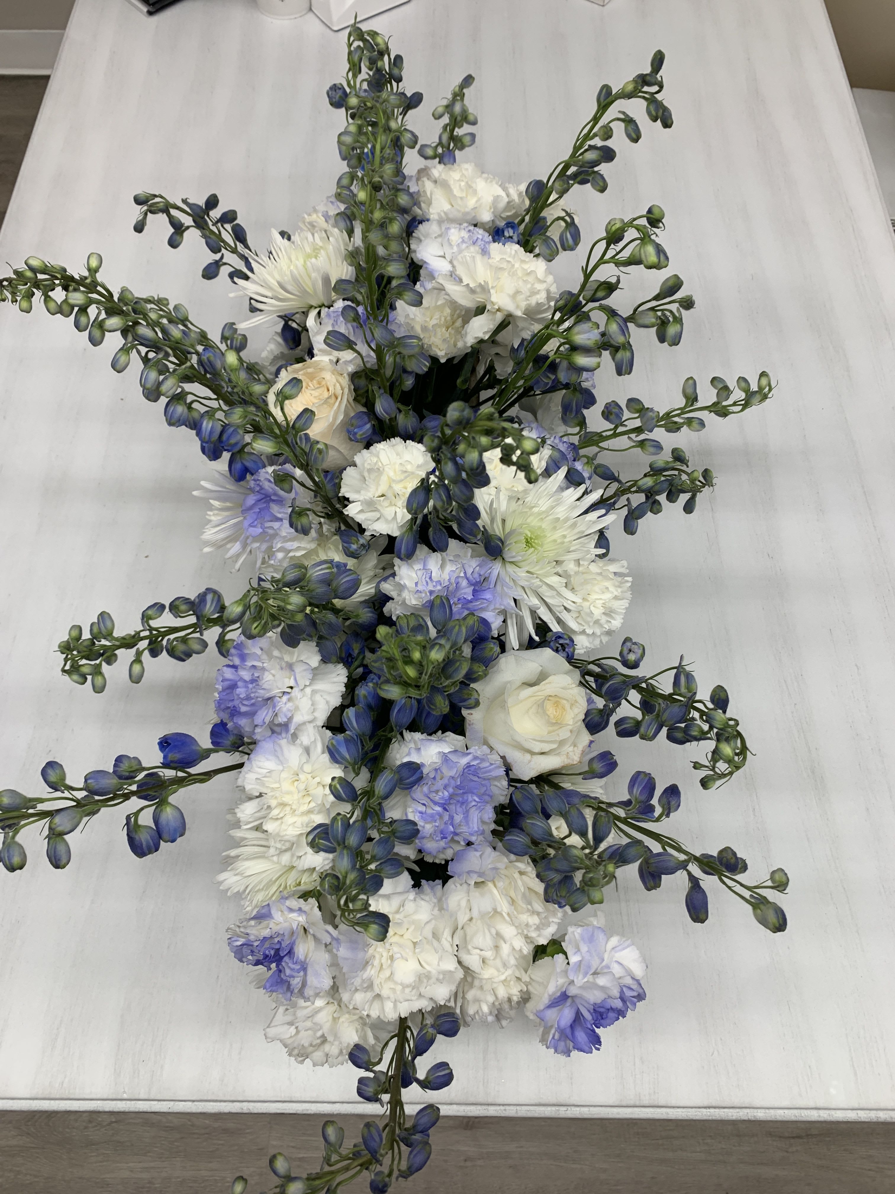 Blue & White Table Centerpiece Blue & White Table Centerpiece - White carnations, daisies and blue accent flower in our long wooden box.