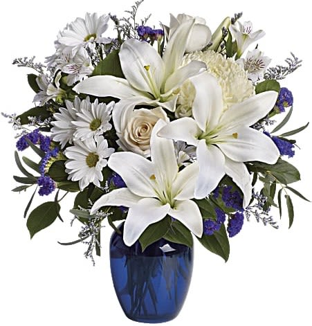 Beautiful In Blue - In this arrangement, the serenity of the color blue along with the purity of intention symbolized by white will let the family know you are sending your calm strength to them during these difficult times.  Beautiful blooms such as blue hydrangea, crème roses, white lilies and alstroemeria along with yellow and white chrysanthemums, eucalyptus, limonium and more are beautifully arranged in a dazzling cobalt blue vase.  Approximately 16 1/2&quot; W x 18&quot; H