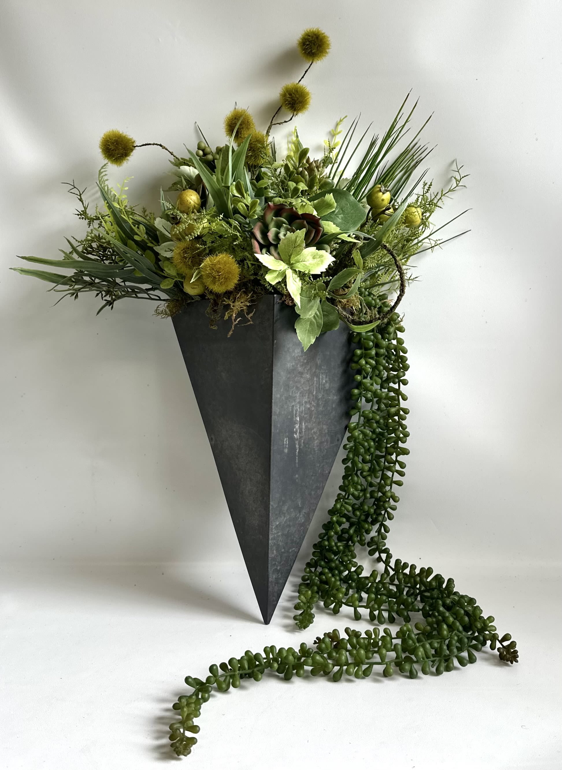 Geo Metal Succulent Wall Arrangement by Barb’s F - Black Metal 14” Container filled with a variety of faux foliage and succulents.  With draping string of pearl (faux) Overall length 48”