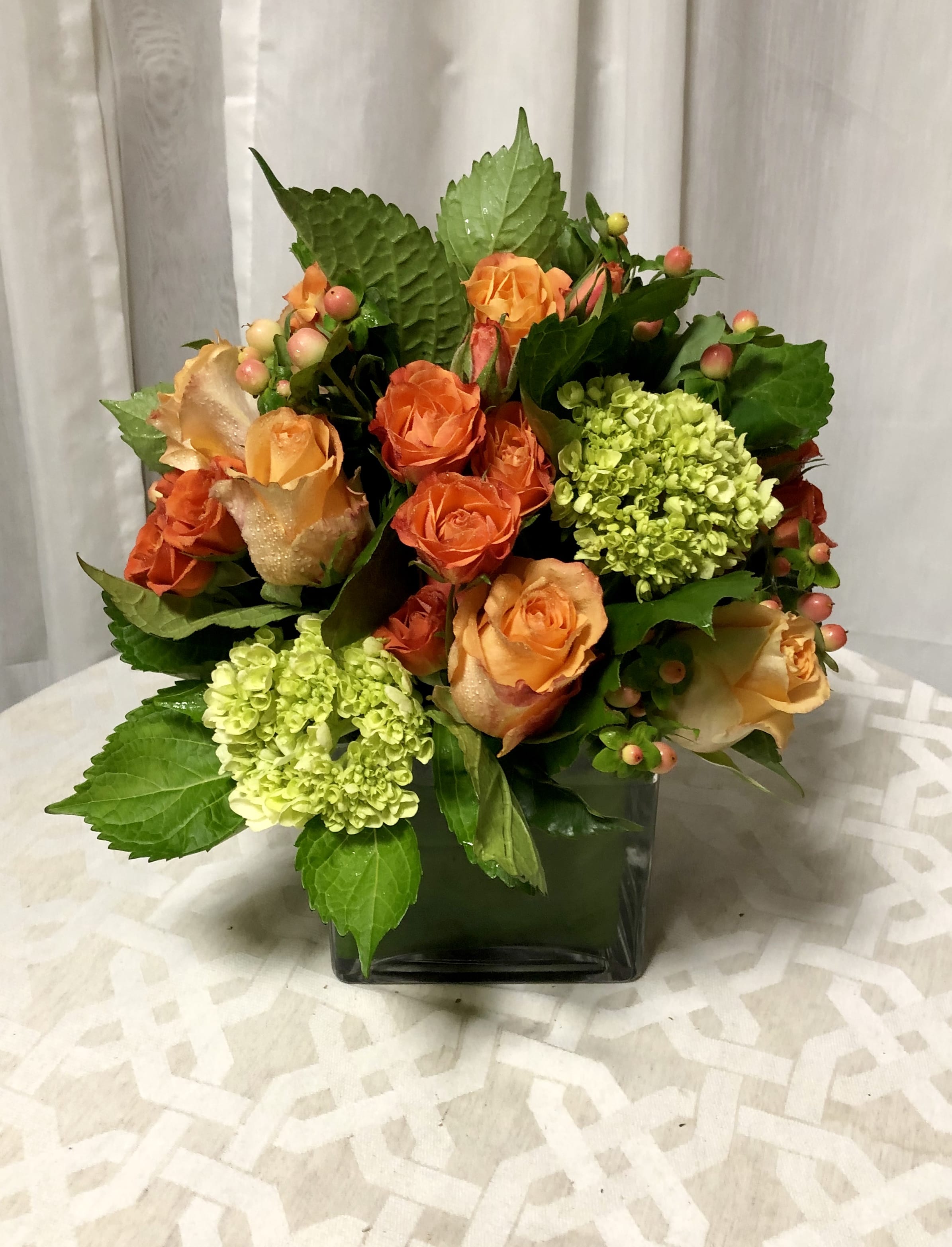 Orange Sherbert - Orange and green have never looked better together ! Orange and rust colored roses compliment bright green hydrangea with fun coffee bean for texture. Set in a low cube for a modern and cool look.   Key notes for this design are roses and hydrangea with a orange and green color palate. 