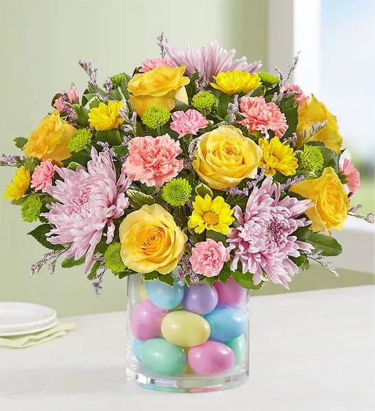 Easter Egg-Stravaganza™ - All-around arrangement with yellow roses and daisy poms, lavender cremons, pink carnations and mini carnations, purple limonium, and green button poms, accented with assorted greenery