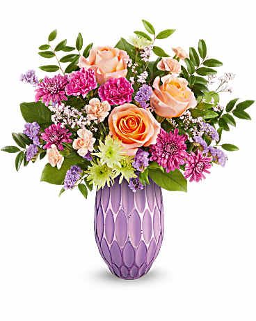 Pretty glow - Peach roses, fuchsia carnations, peach miniature carnations, green cushion spray chrysanthemums, purple cushion spray chrysanthemums, purple sinuata statice, and pink limonium are artfully arranged with huckleberry and salal in Teleflora's Pretty Glow vase, creating a stunning Mother's Day bouquet.   