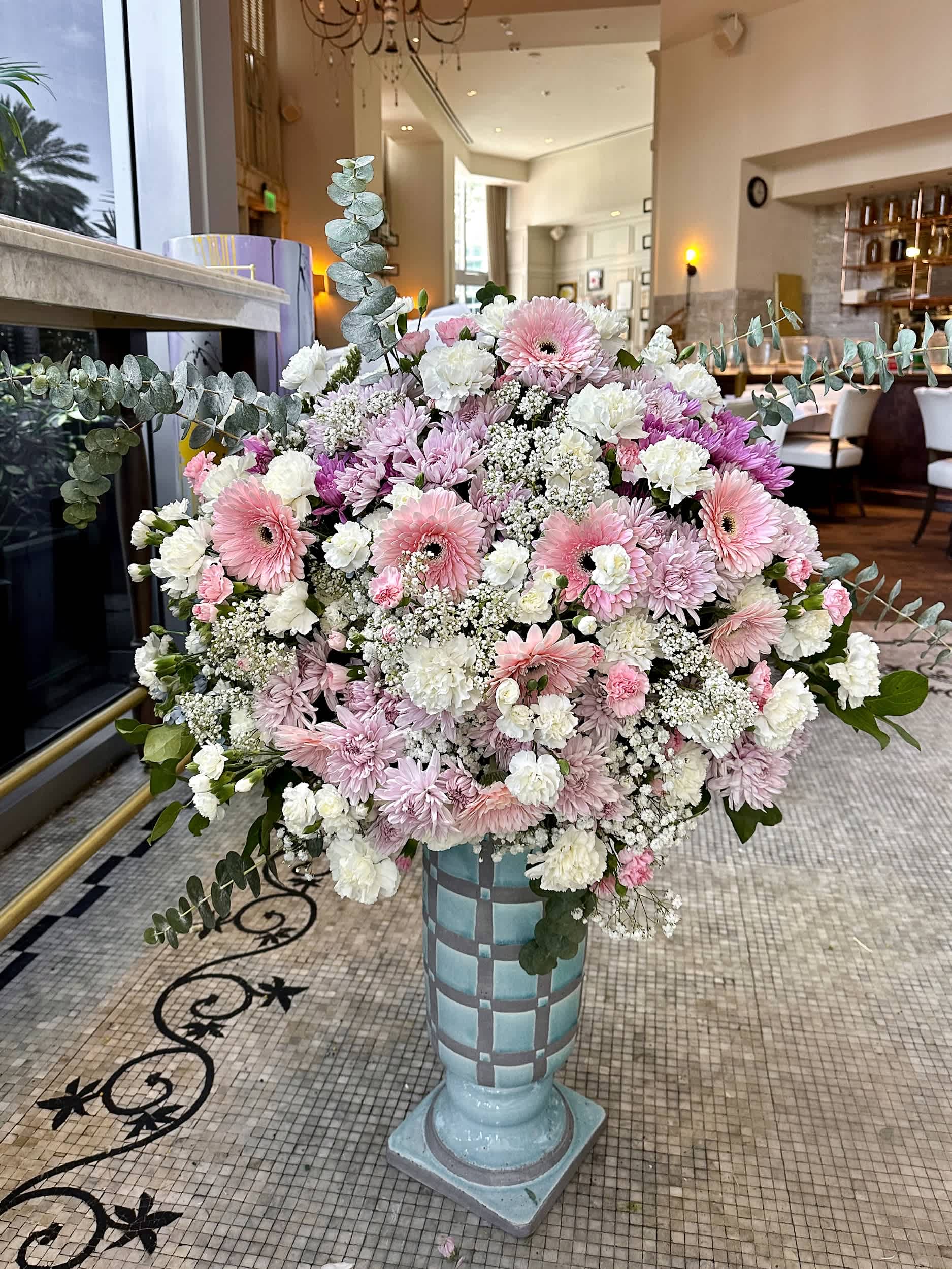 Grand Pastel Symphony Vase - Transform any space with the &quot;Grand Pastel Symphony Vase.&quot; This expansive arrangement showcases a delicate mix of pink and white gerbera daisies, chrysanthemums, carnations, and more, all elegantly arranged in a tall, artistic vase. The soft, pastel hues create a serene and inviting atmosphere, perfect for grand events and luxurious interiors. Please note, vase styles may vary slightly – contact us for current options.  Arrangement Details: Main Flowers: Gerbera Daisies, Chrysanthemums, Carnations, Eucalyptus, Other Premium Blooms Container: Tall artistic vase (styles may vary, please call for current options) Approximate Dimensions: 20&quot;D x 42&quot;H