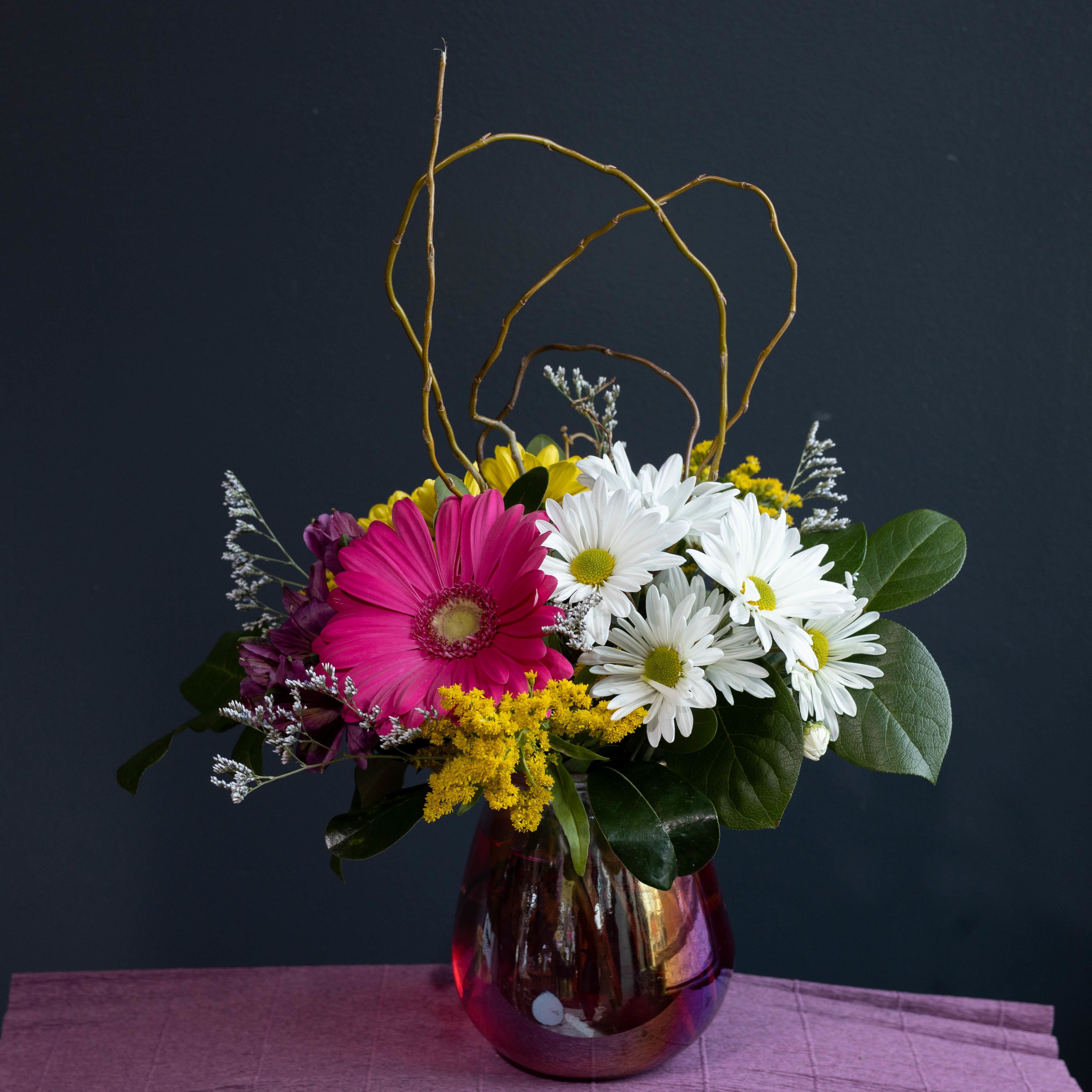 Oopsie Daisy - A fun playful arrangement filled with a variety of daisies and other flowers that brings the freshness of spring all designed in a pink iridescent vase!