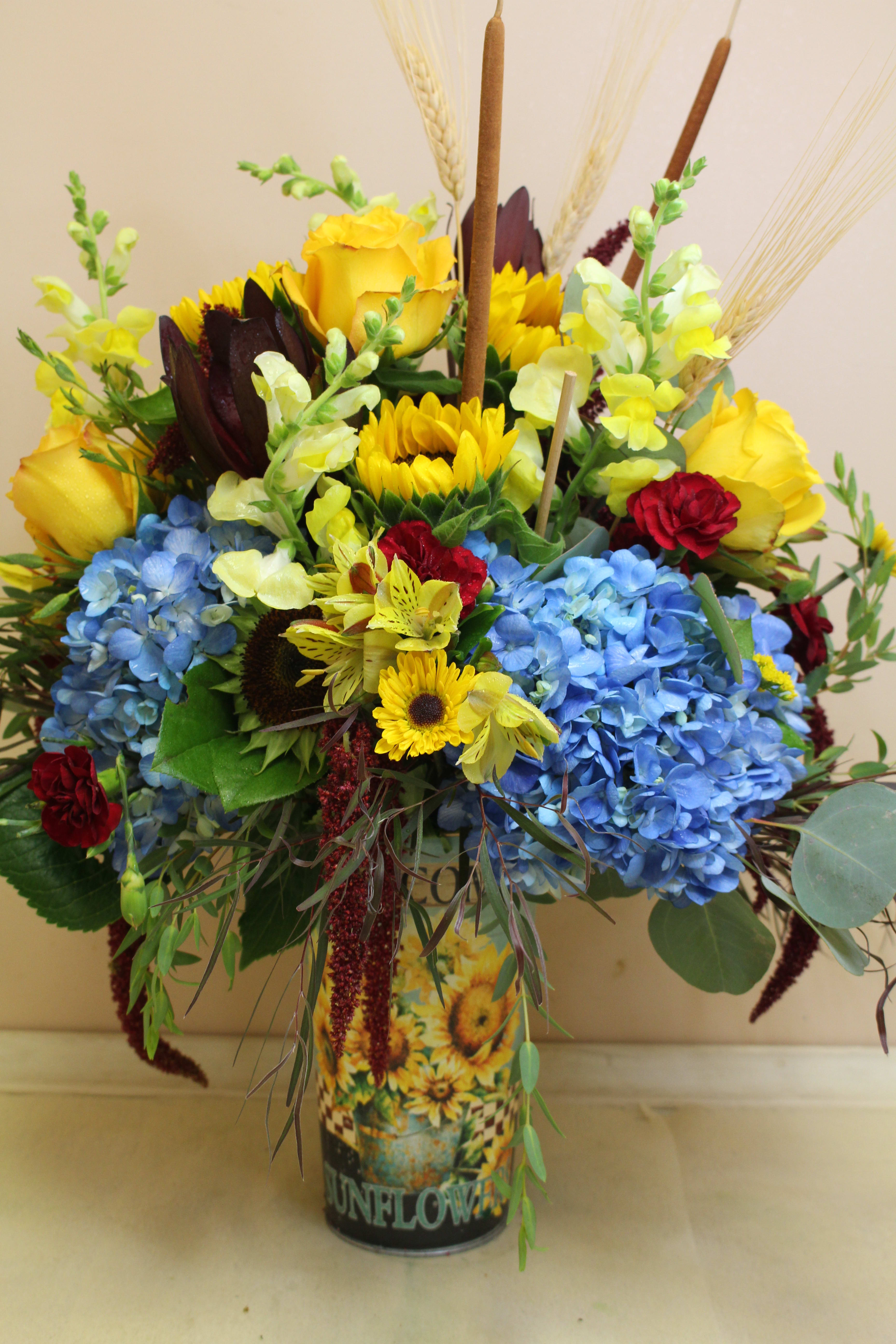 Welcome sunflower galvanized cylinder  - A different take on fall, blue hydrangea, sunflowers and a beautiful fall mix  fill this galvanized sunflower container.  sure to please!