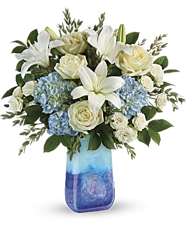 Ocean Sparkle Bouquet Ocean Sparkle Bouquet - Like a calm morning by the sea, this beautiful bouquet of blue and white blooms arranged in a stunning, hand-blown art glass keepsake vase, invigorates and inspires. This beautiful bouquet includes blue hydrangea, white roses, white spray roses, parvifolia eucalyptus, and lemon leaf. Delivered in a Blue Lapis Gemstone Art Glass vase. Orientation: All-Around VASE Like an ocean sunset, this bold bouquet of radiant sunflowers and orange roses in a hand-blown art glass vase invigorates the soul!