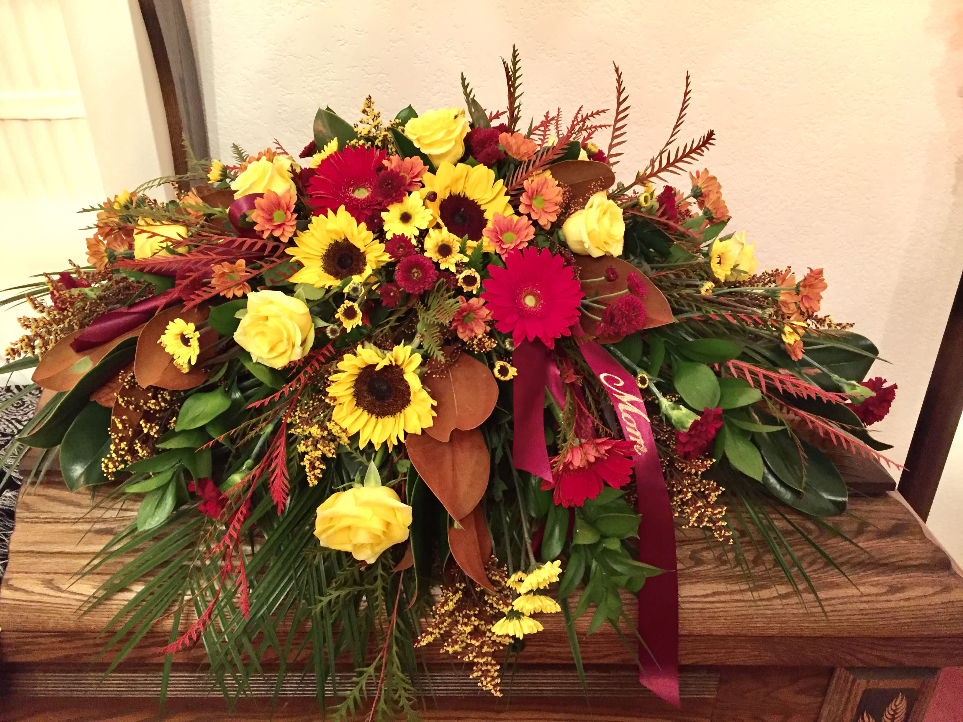 Jewel Tones Casket Spray Jewel Tones Casket Spray - Yellow roses with burgundy mums, carnations, sunflowers, vykings, magnolia and grevellia foliages