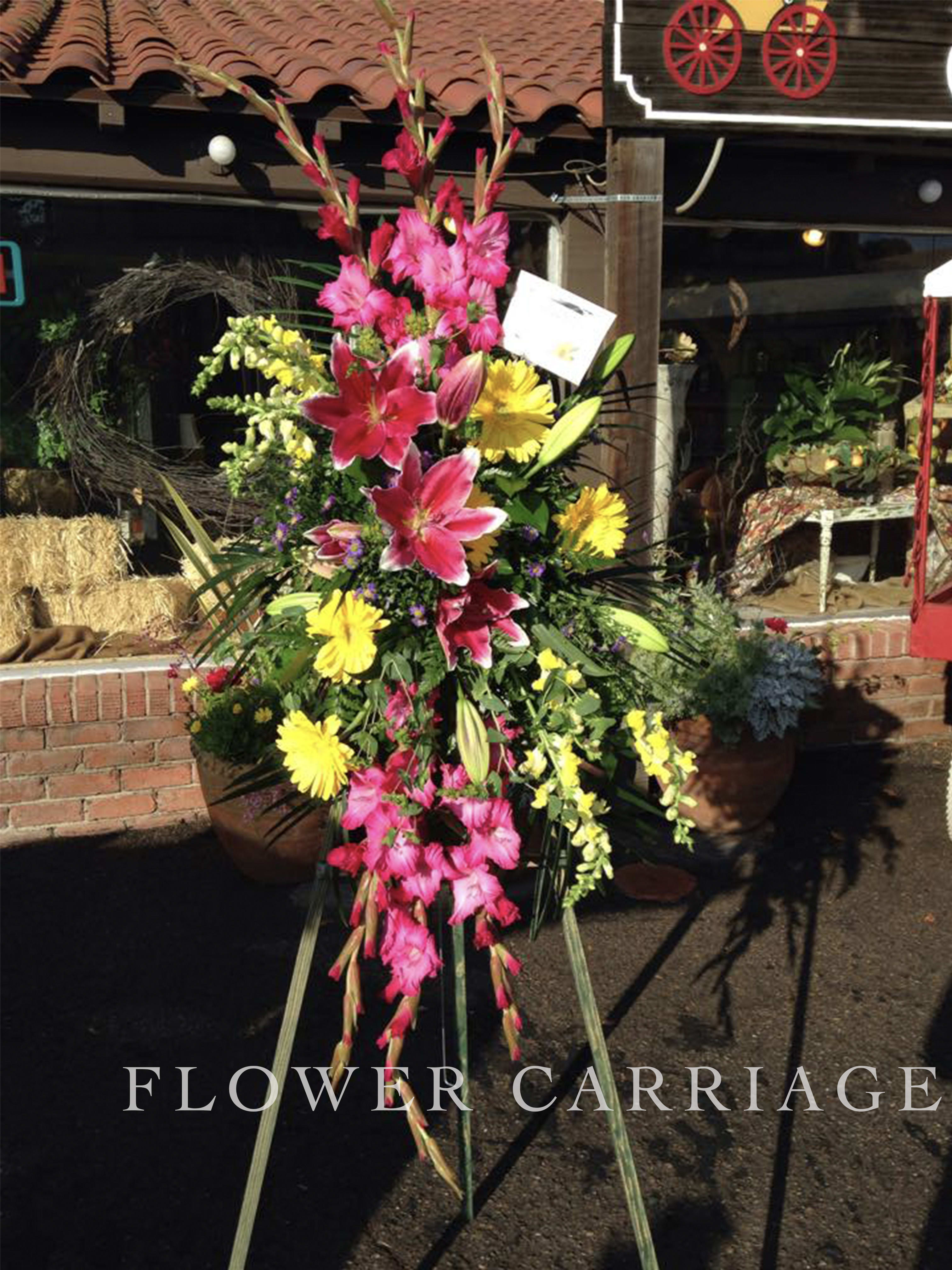 Bright Rainbow Spray By Flower Carriage Bright Rainbow Spray By Flower Carriage - The bright main colors of this arrangement will help celebrate the special person. This easel features: Star Gazers, Gladiolus, Gerber Daisies, Snap Dragons and greenery.