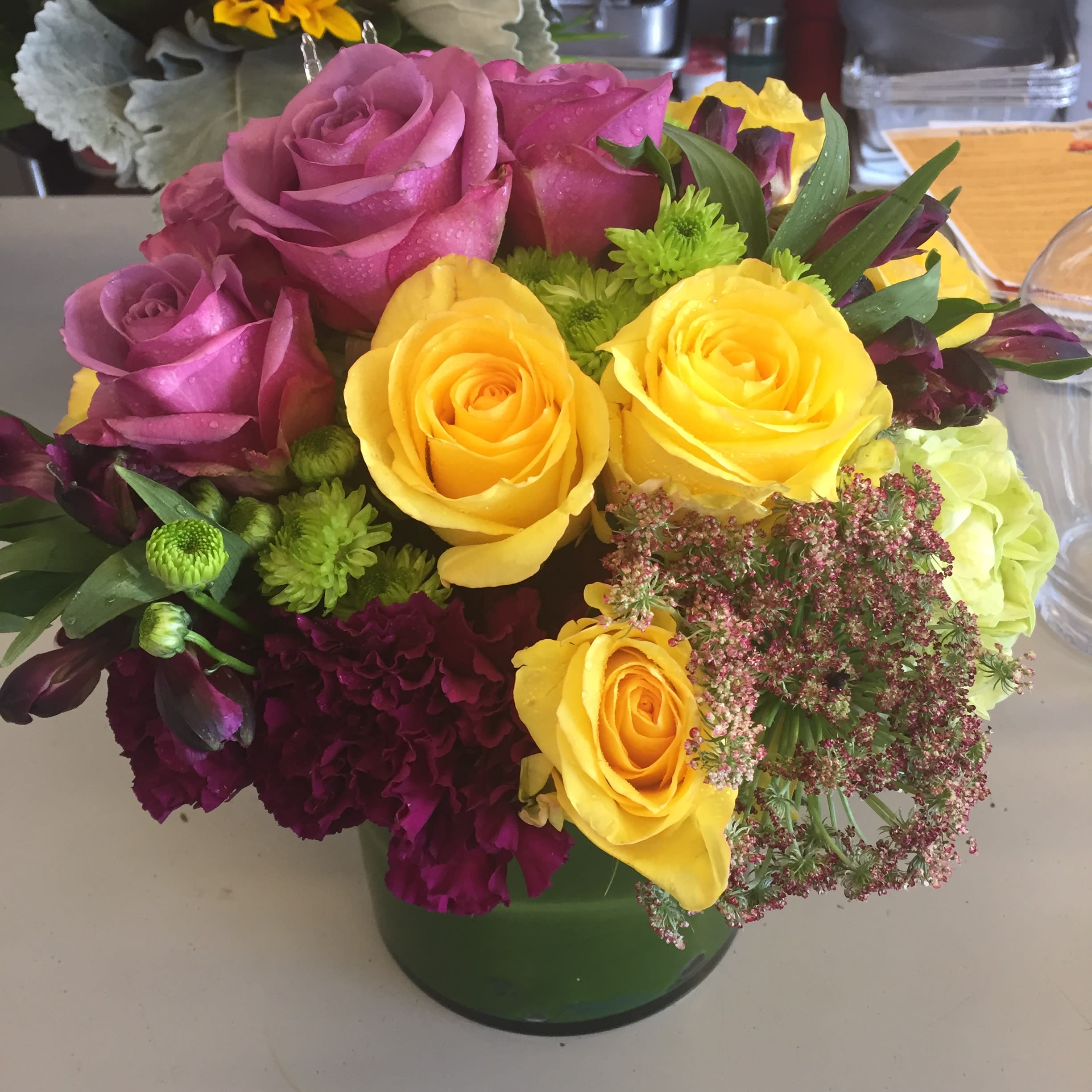 Lavender and Yellow Roses with Accents - A lovely combination of lavender roses, yellow roses and seasonal accents in a clear glass vase.  A compact style that is perfect for a centerpiece. 