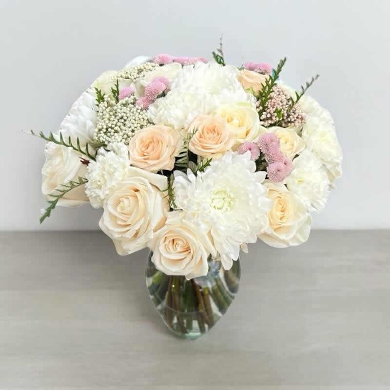 White Poms With Roses In A Vase #67 - This enchanting floral arrangement combines the delicate allure of white poms with the classic beauty of roses. The white pom flowers, known for their lush, round blooms, create a backdrop of purity and elegance. Complementing them, the roses—available in an array of captivating colors such as vibrant red, soft pink, or creamy white—add a touch of timeless romance. Arranged thoughtfully in a clear glass vase, this bouquet is a perfect blend of simplicity and sophistication. Whether as a gift or a centerpiece, this arrangement is designed to bring joy and elegance to any space.