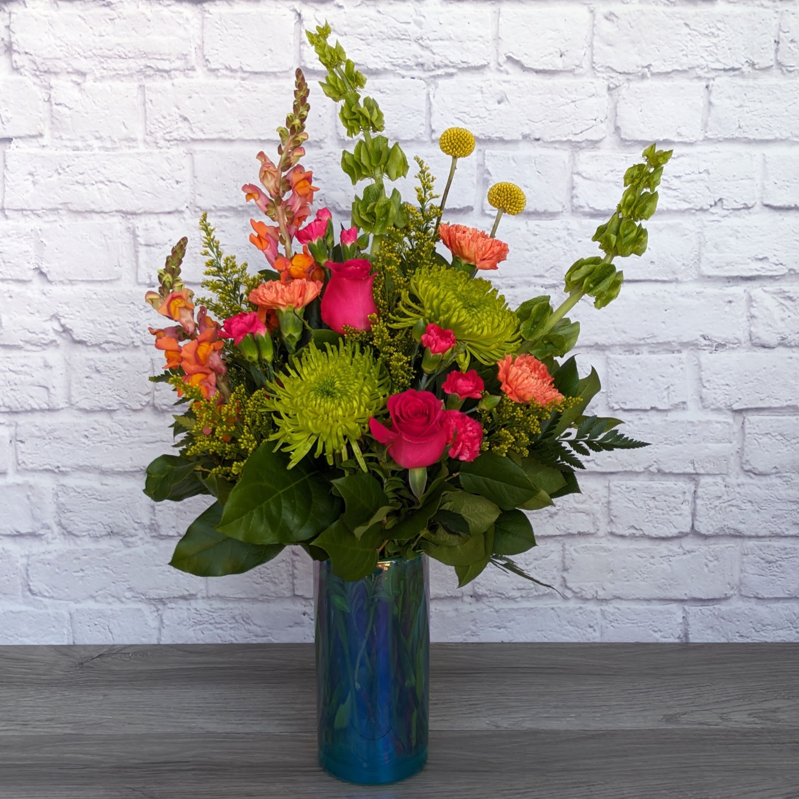 Citrus Daydream - Citrus Daydream is A Ladybug Floral exclusive bouquet. Featuring bells of Ierland, snapdragons, craspedia, spider mums, roses, carnations, mini carnations, and solidago in classic citrus colors. All featured in a 8” aqua glass vase with iridescent finish.  One Sided Orientation 26&quot;H X 18&quot;W  