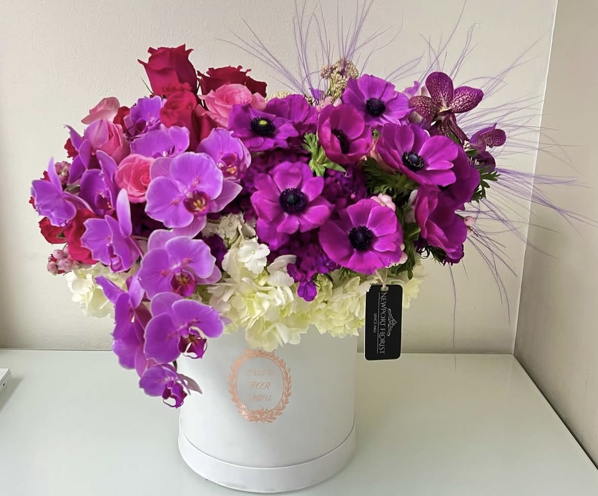 Magenta Romance NF-Y9 Magenta Romance NF-Y9 - This lush floral design is teeming with shades of beautiful hot pink roses and next to them a cascade of phalaenopsis orchids and a cluster of gorgeous magenta anemone blooms resting over a cloud of white hydrangeas and fine plum color pampas shooting out on the right side all arranged in a mid size white gift box. Perfect for a Birthday Gift.