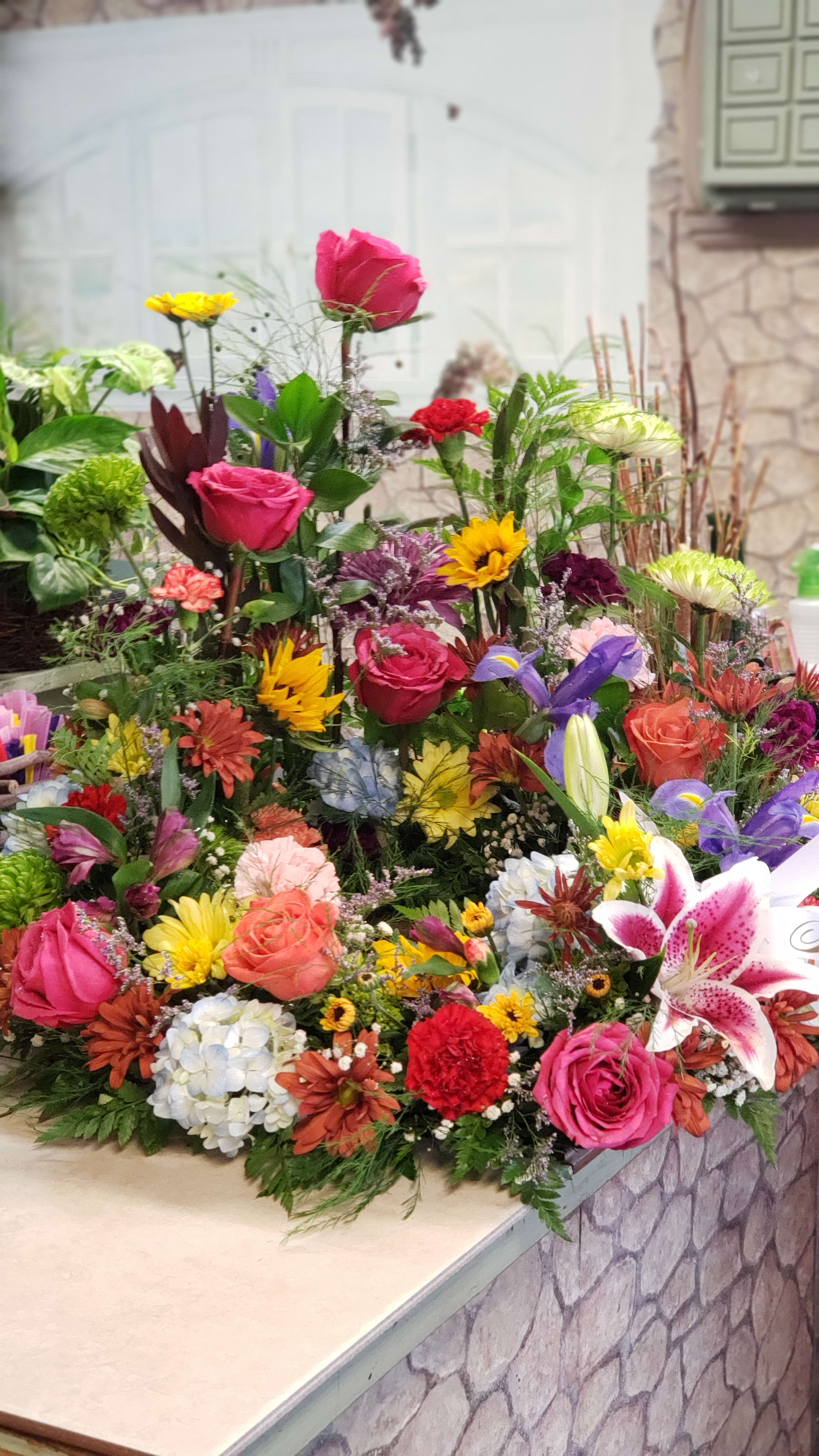 Urns Tribute Ring  - A stunning bold &amp; bright mix of market fresh flowers in stock at time of order &amp; time sensitive leeway before the service.  Flowers &amp; colors, rose CM size &amp; in stock colors can vary.  The Urn of Ashes nest into the center of the ring...with a &quot;garden theme&quot; background.  Fits up to 10-11&quot; wide, 7-9&quot; tall for center urn or box to nest freely.  Script on bow is an additional $4.00 per script.  