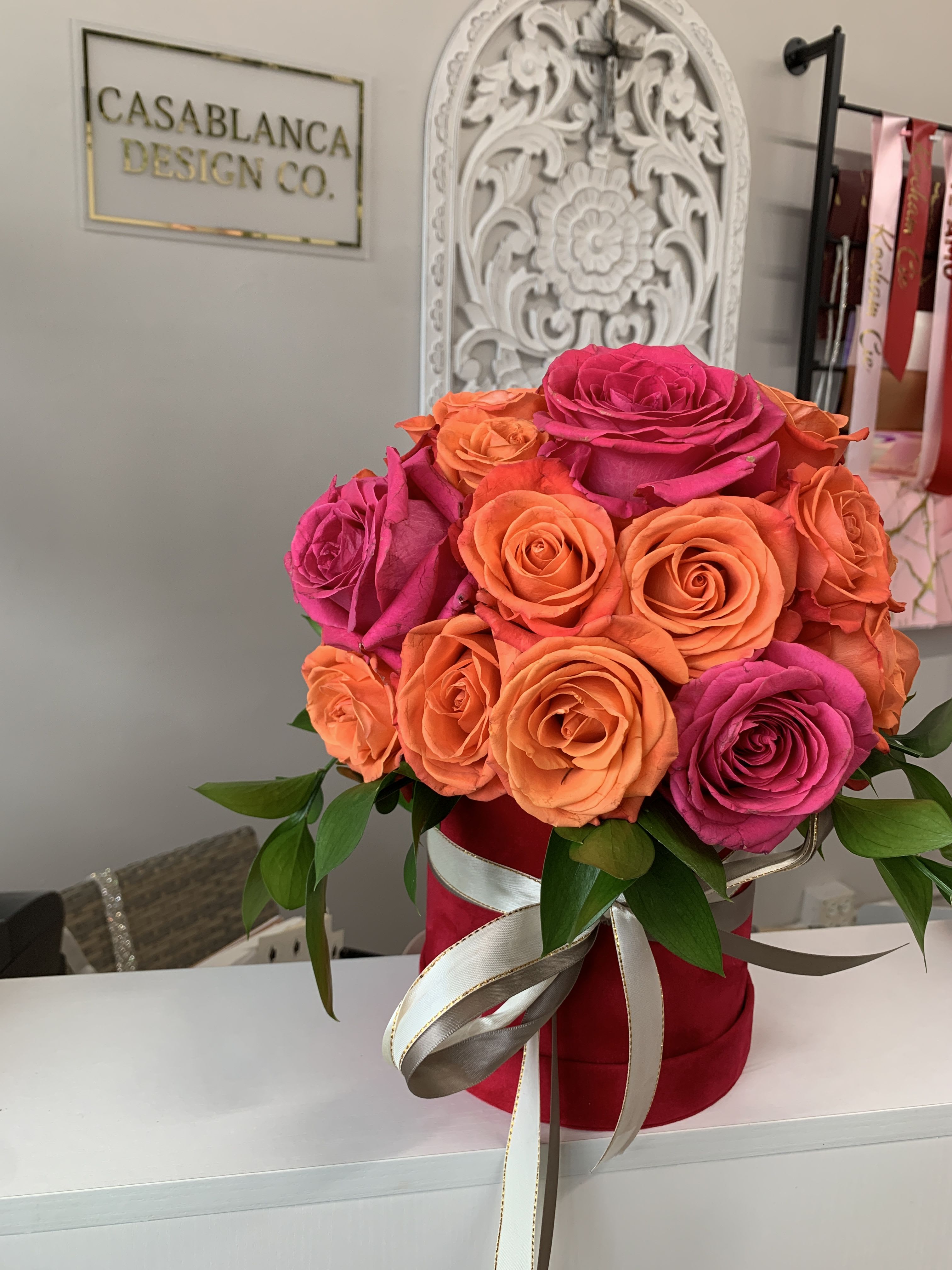 Moana Moana - Orange and hot pink roses with ranunculus in a red velvet or beige box with taupe ribbon.