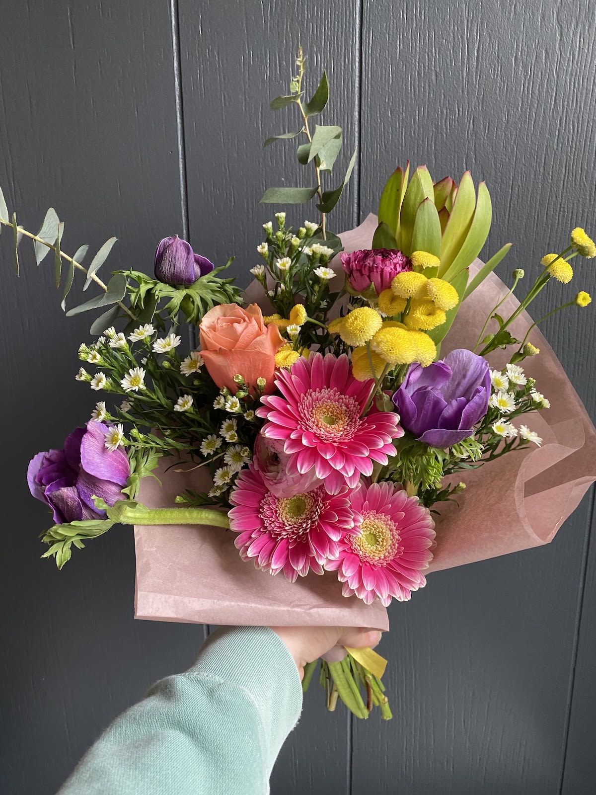 SEASONAL WRAPPED BOUQUET - Seasonal, colorful flowers and foliage wrapped in floral paper. No vase included.  Year round flowers that we typically stock: specialty rose, spray rose and garden rose, ranunculus, anemone, gerbera daisy, protea, lisianthus, chrysanthemum, larkspur, snapdragon, delphinium, stock, aster, dianthus, hypericum, feverfew, astrantia, leucodendron