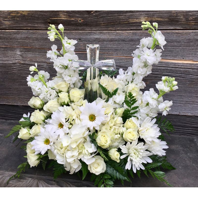Crystal Cross in White - An eloquent arrangement featuring at its' center, a beautiful glass crystal cross.  It is then surrounded by a variety of fresh white flowers such as carnations, cushion mums, snapdragons, white roses, and baby's breath.  Other white seasonal flowers will be available as well, depending on the time of year ordered.    A fitting tribute to your loved one and something the family can take home and save as a keepsake of the memorial.  Other colors are easily available upon request.  Just let us know your choice of colors when placing your order.