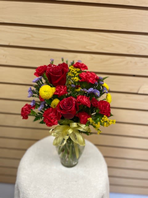 Patterson - Small mixed cut with red roses, red mini carnations, yellow billy bob, purple monte casino, and yellow solidago in a vase with a bow