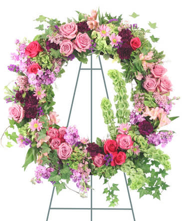Ever Enchanting - Easel Large Wet Floral Foam Wreath Foliage: Variegated Pittosporum, Ivy Purple Statice Lavender Roses Hot Pink Roses Lavender Stock Green Hydrangea (Cut Apart) Pink Alstroemeria Pink Waxflower Bells Of Ireland Purple Carnations Lavender Daisy Poms