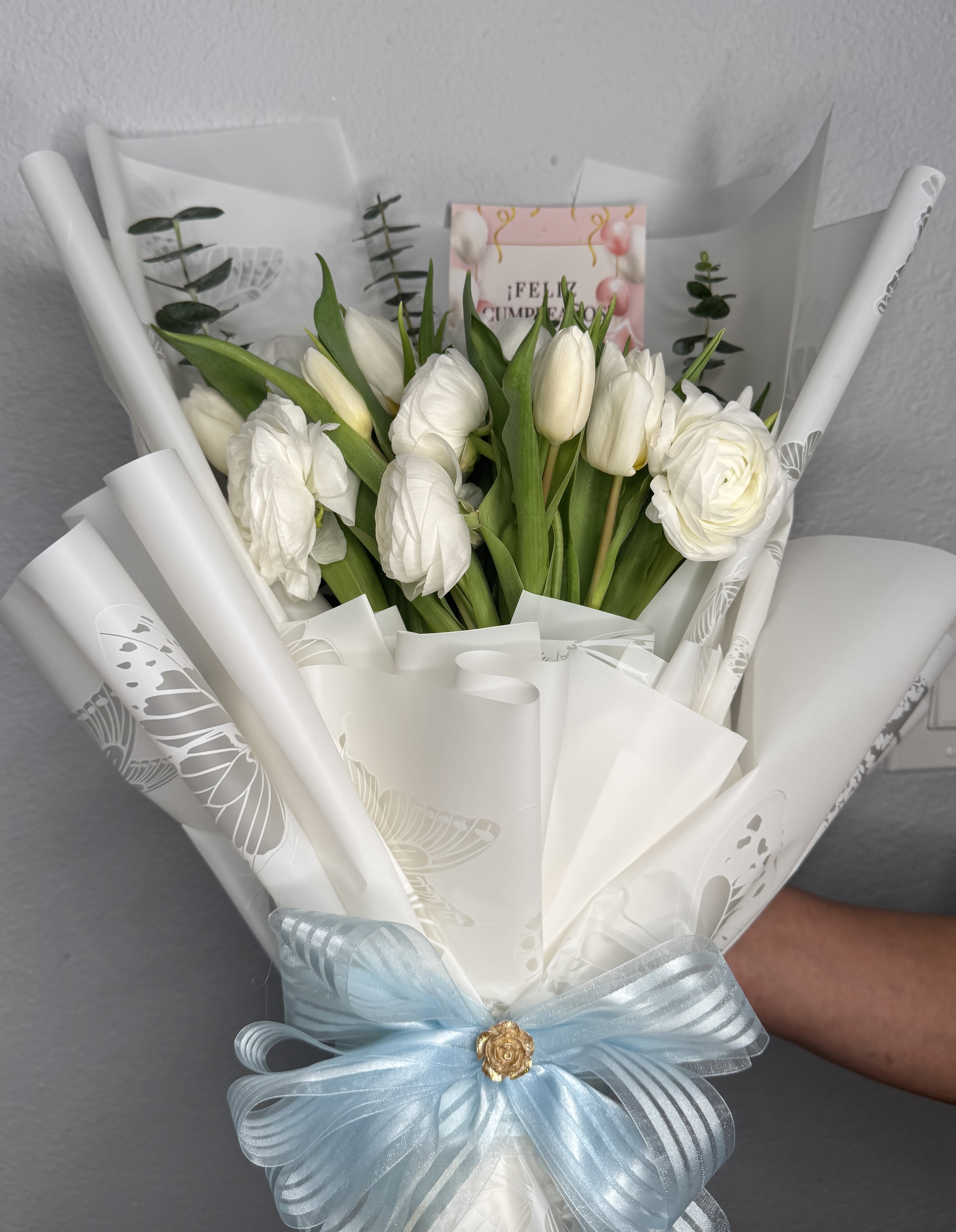 Elegant Whisper Bouquet - A graceful arrangement of pure tulips and ranunculus, delicately paired with soft eucalyptus accents. Wrapped in luxurious white floral paper with butterfly details and finished with a bow, this bouquet is the perfect symbol of elegance, peace, and heartfelt wishes. Ideal for birthdays, new beginnings, or simply to express purity and affection with timeless style.  Includes:  Fresh tulips  ranunculus eucalyptus stems premium wrap  satin ribbon