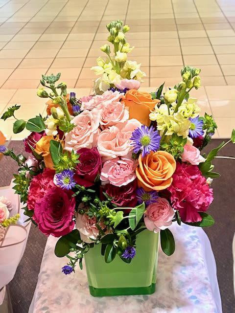 Spring fresh - 4 each roses, 50cm, Orange 2 stems roses, spray, hot pink 3 stems carnations, miniature, pink 3 each stock, light yellow 1 stem asters, monte cassino, large, purple 1 stem pink spray Rose 1/2 stem bupleurum 1/3 block floral foam Green cube Vase 