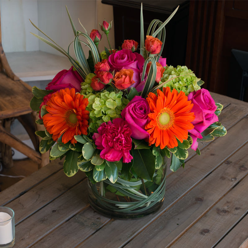 Citrus Splash - Vibrant arrangement in hot summer colors. Gerbera, green hydrangea, roses, spray roses, lily grass, and other flowers are sure to bring a smile to anyone's face.