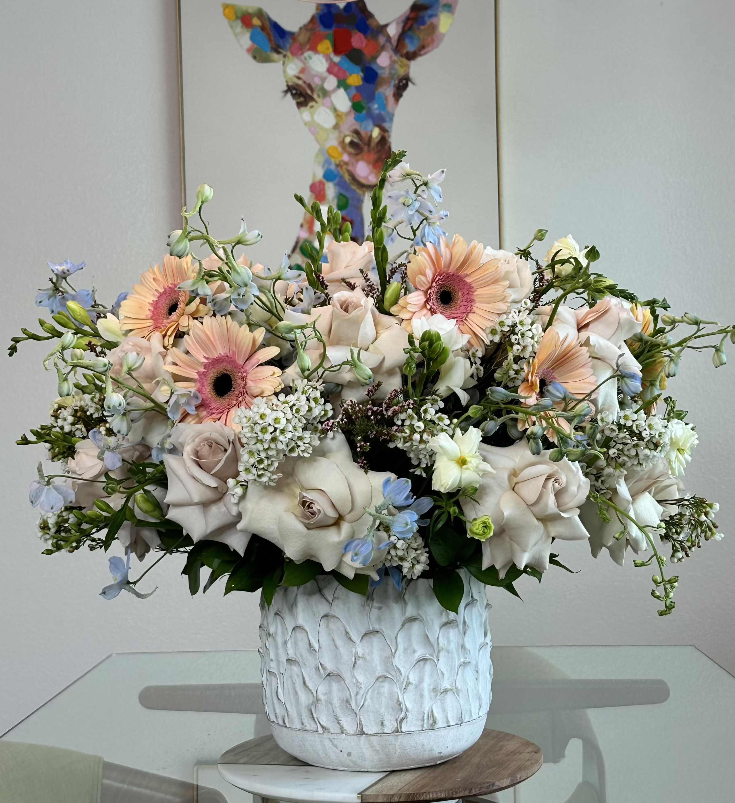 Petala and Friends  - Garden-style arrangement featuring blush roses, peach gerbera daisies, delicate delphiniums, and lush greenery in a ceramic vase.