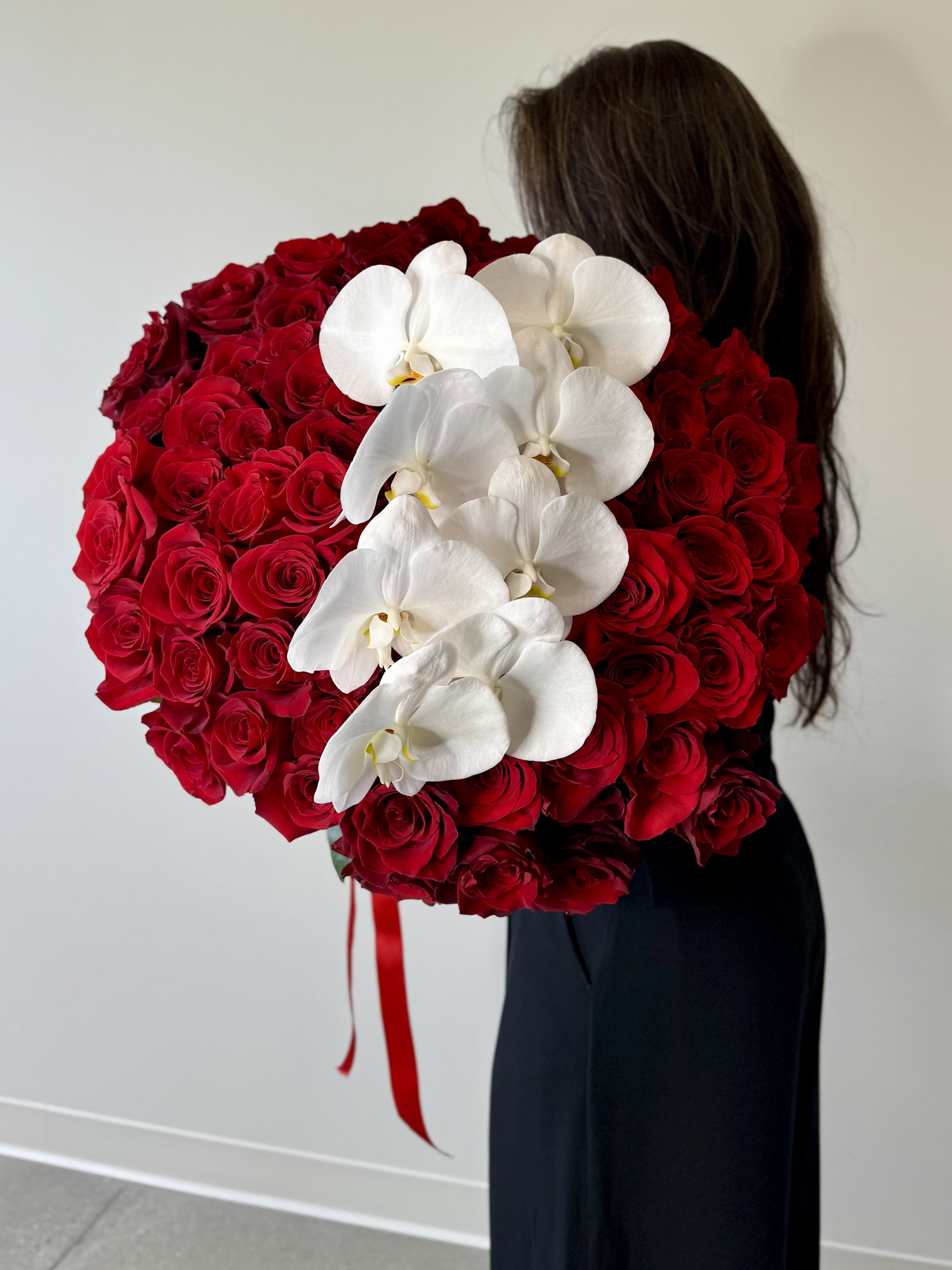 Extraordinary Love - A tale of opulence and grandeur unfurls here, where only the most regal souls dare to dream. Behold a masterpiece that commands awe: 100 long-stemmed red roses, crowned with the majestic embrace of a phalaenopsis orchid, presented in a towering clear cylinder vase. This is luxury redefined—a coveted treasure, with Deluxe at 125 stems and Premium soaring to 150 stems. Note its splendor requires three days’ advance order, a testament to its bespoke magnificence.    Red roses reign supreme, their velvety depths a bold proclamation of passion, devotion, and timeless adoration, each stem stretching long and proud. At their pinnacle, a phalaenopsis orchid blooms in radiant elegance, its pristine petals exuding purity, grace, and an eternal vow—royalty among flowers. Together, they craft an arrangement that’s not merely a gift, but a coronation of love, a lavish gesture to sweep your beloved into a world of extravagance. This is the bouquet for those who live grandly, who deserve nothing less than the extraordinary.    Step into this floral kingdom at Irvine Village Flowers. Visit us online or in-store, and let our exquisite delivery across Irvine bring this spectacle to life, arriving fresh and resplendent. A story of luxury, written in every regal bloom.