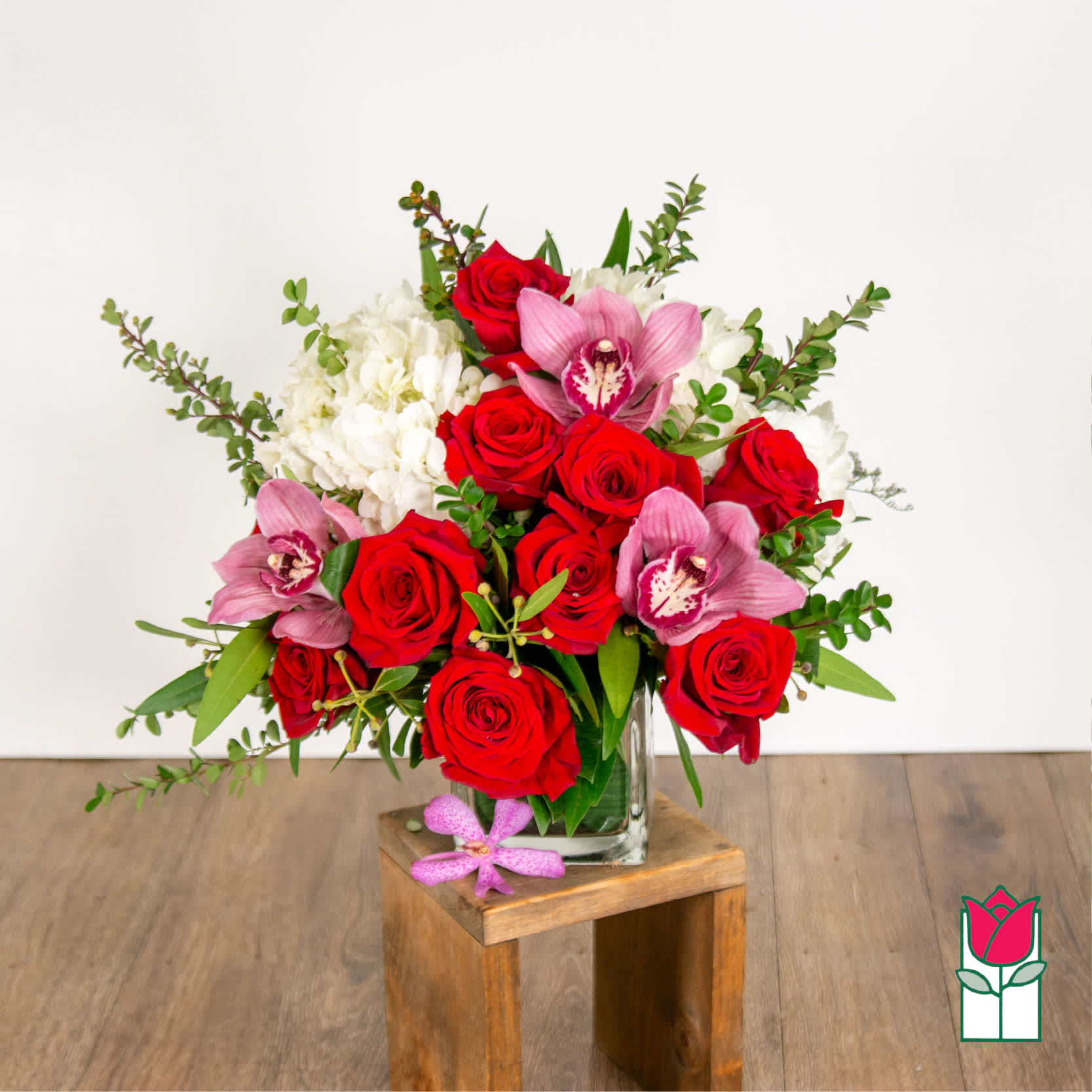 Beretania's Olivia Bouquet (Red Rose &amp; Pink Cymbidium) [Hue Varies] - Elevate your space with the Beretania Florist Compact Bouquet, a charming floral arrangement that effortlessly combines elegance and versatility. Housed in a beautiful 4&quot; glass cube vase, this compact bouquet features a delightful composition of hydrangeas, foliage, and your choice of roses in various colors, allowing you to tailor it to your preferences.  Whether you opt for the timeless allure of red roses, the soft romance of pink, or the vibrant cheerfulness of yellow, each variant of the compact bouquet brings a unique charm to any setting. The meticulous design ensures a harmonious blend of textures and hues, creating a visually appealing arrangement that suits any occasion.  For those seeking an extra touch of sophistication, consider our upgraded option – the Olivia Compact Bouquet. This variant remains true to the original design but introduces the exotic beauty of colorful cymbidium orchid blossoms, elevating the bouquet to a new level of elegance.  Perfect as a thoughtful gift or a stunning addition to your own space, the Beretania Florist Compact and Olivia Bouquets are crafted with precision and care, promising a burst of floral beauty that suits your style and preferences. Choose the color that speaks to you and let the timeless beauty of these bouquets brighten your day. 