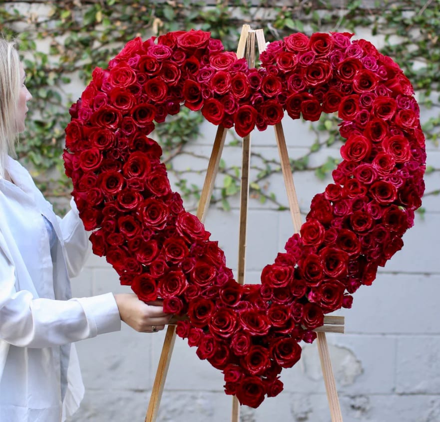 Heart stand Red - The love for someone who has passed away lives on forever in the hearts of those left behind. This sentiment is best captured with our standing, open heart-shaped red floral arrangement. Handcrafted by our caring florists with red roses and orchid.