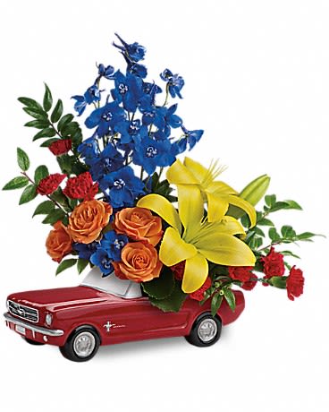 Living The Dream '65 Ford Mustang - This colorful arrangement includes orange spray roses, yellow asiatic lilies, red carnations, red miniature carnations, blue delphinium, galax leaves and huckleberry. Delivered in a '65 Ford Mustang collectible keepsake.