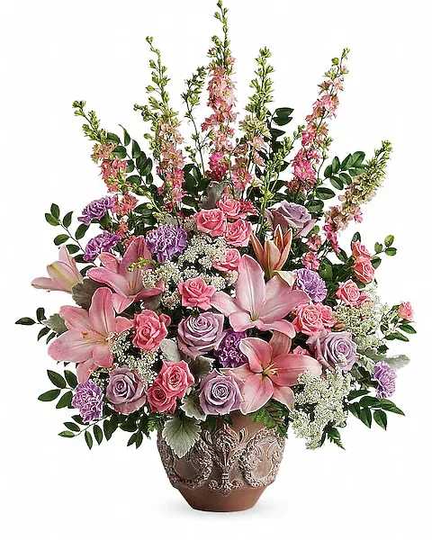 Soft Blush Bouquet - A touching tribute to a beloved woman, this beautiful, soft pink and lavender arrangement is presented in a large antiqued pot for an elegant touch. This soft pink arrangement features lavender roses, pink spray roses, pink asiatic lilies, lavender carnations, pink larkspur, queen anne's lace, huckleberry, dusty miller, and leatherleaf fern. Delivered in a Classical Garlands pot.  