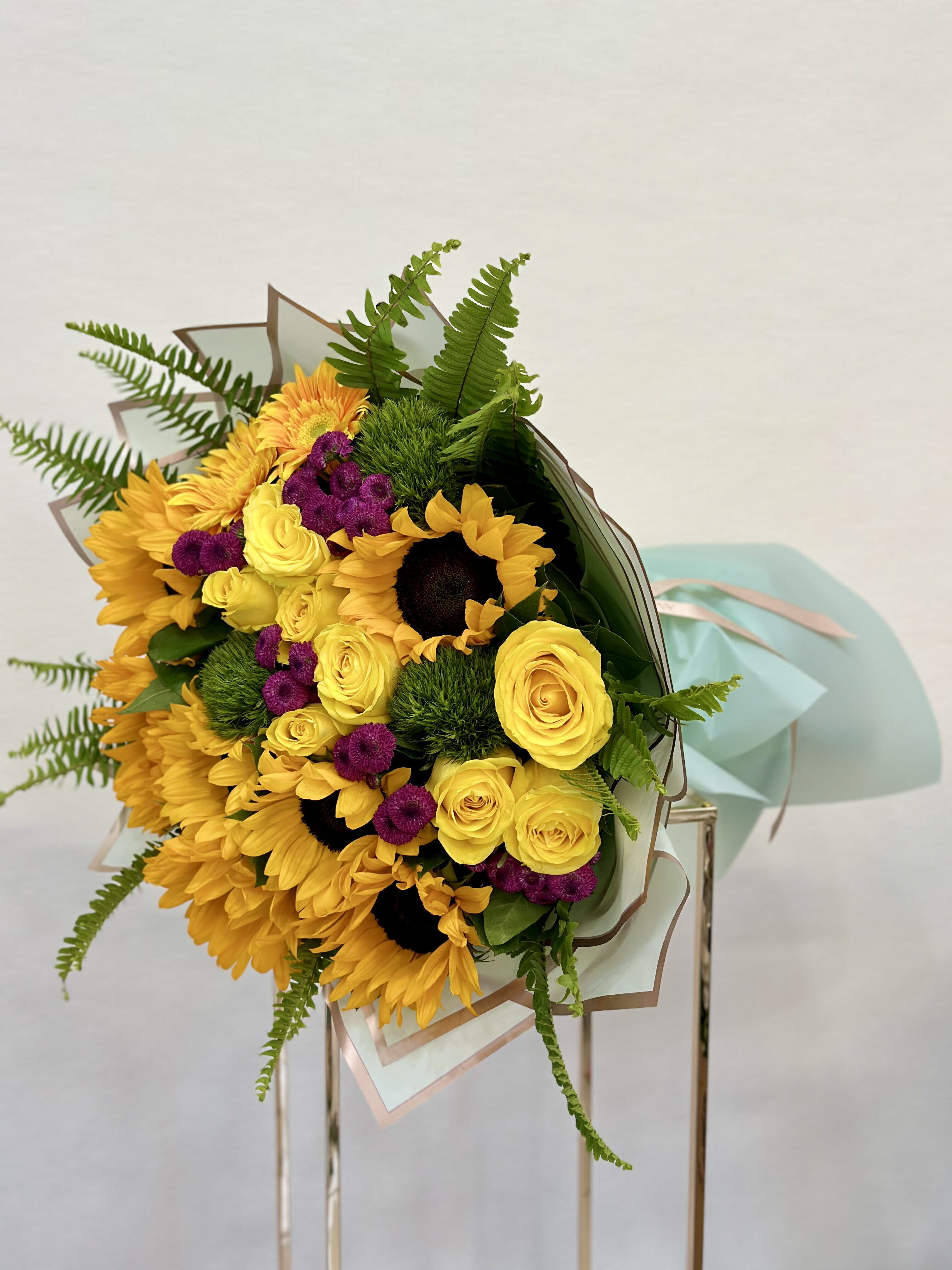Sunflower Bliss Bouquet - Bursting with the warmth of golden sunflowers, the tender elegance of yellow roses, and the regal charm of purple chrysanthemums, this bouquet is a symphony of color and beauty. Whether it's to celebrate a special occasion or simply to brighten someone's day, this bouquet is sure to evoke smiles and spread warmth wherever it goes. 