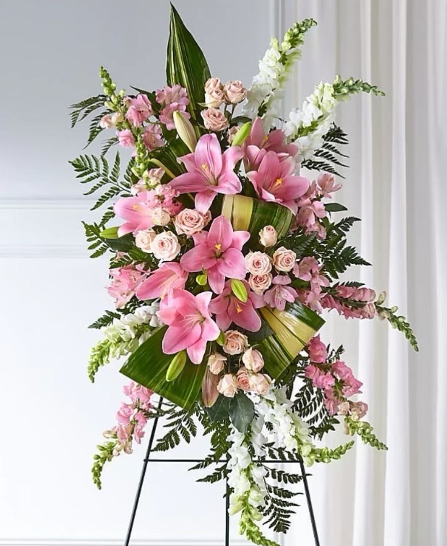 ELEGANT EMBRACE STANDING SPRAY - Our Elegant Embrace Standing Spray shares the warmth and comfort your loved ones need during this difficult time through each blushing bloom. A local florist beautifully combines lilies, spray roses and snapdragons with greens to express your heartfelt love.  Includes: • Pink Lilies • White Snapdragons • Pink Snapdragons • Pink Alstoremeria • Pink Spray Roses • Variegated Aspidistra • Leatherleaf Fern • Personalized Card Message
