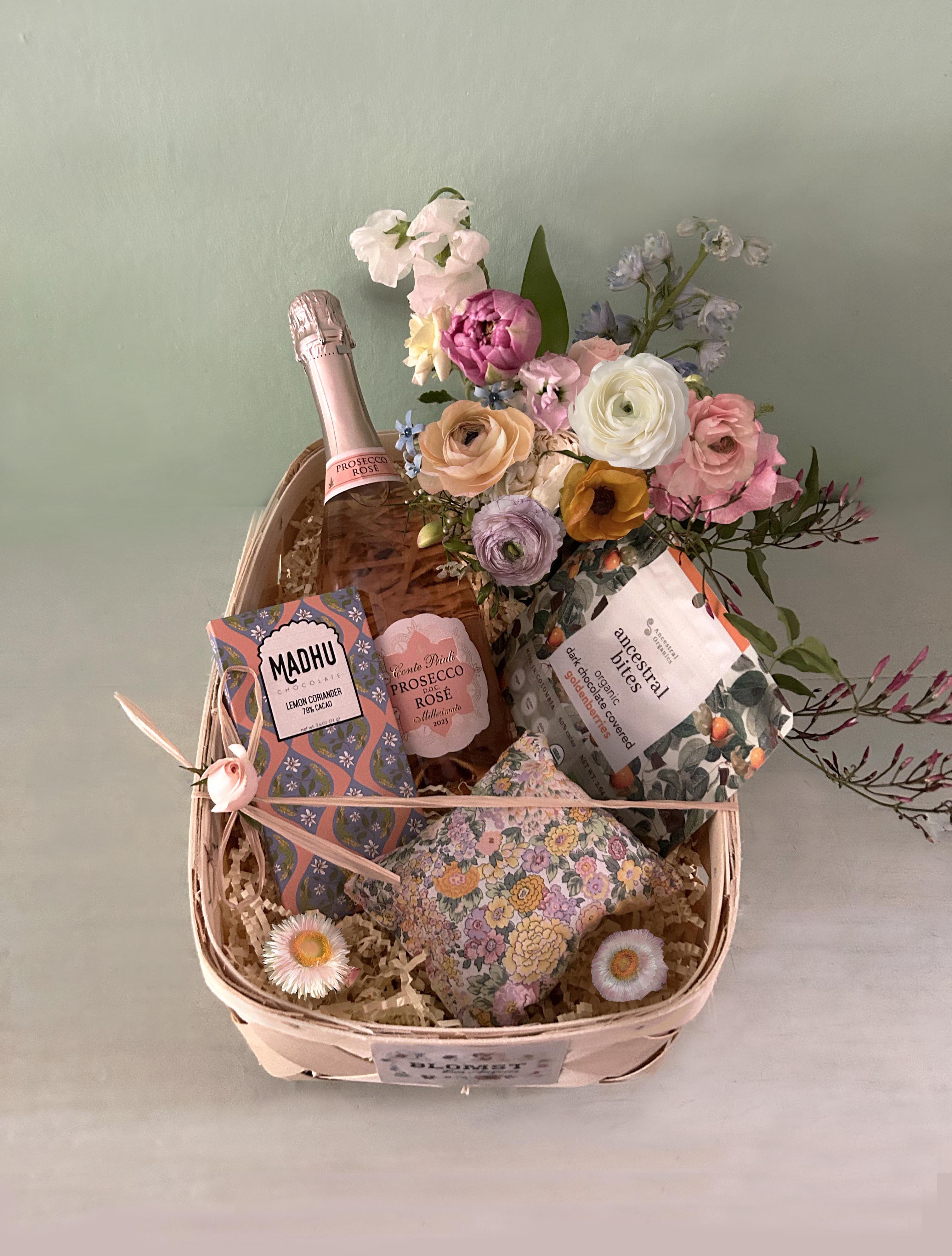 Bubbly Basket - A celebration box with bubbly, chocolate, fresh flowers and a Liberty x Blomst sachet of dried flowers.  Sparkling Prosecco Rosé wine that is made from both Glera (Prosecco) and Pinot Noir grapes. Vegan Lemon Coriander chocolate bar - 78% Cacao. In this bar, lemon is paired with the citrusy, herbaceous notes of coriander seed. The result is a very unique, aromatic dark chocolate bar.  Organic Dark Chocolate Covered Goldenberries, healthy and sustainable superfood. Liberty fabric sachet of scented natural lavender flowers for the drawer Adorned with a mini Blomst LA bouquet in a small cylinder vase All placed in a wooden square box or wooden basket (10 by 10 by 4).